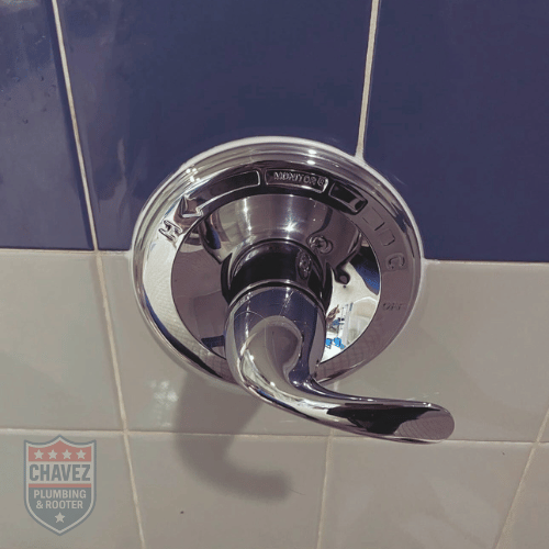 Close-up of a chrome bathroom faucet handle mounted on a tiled wall.