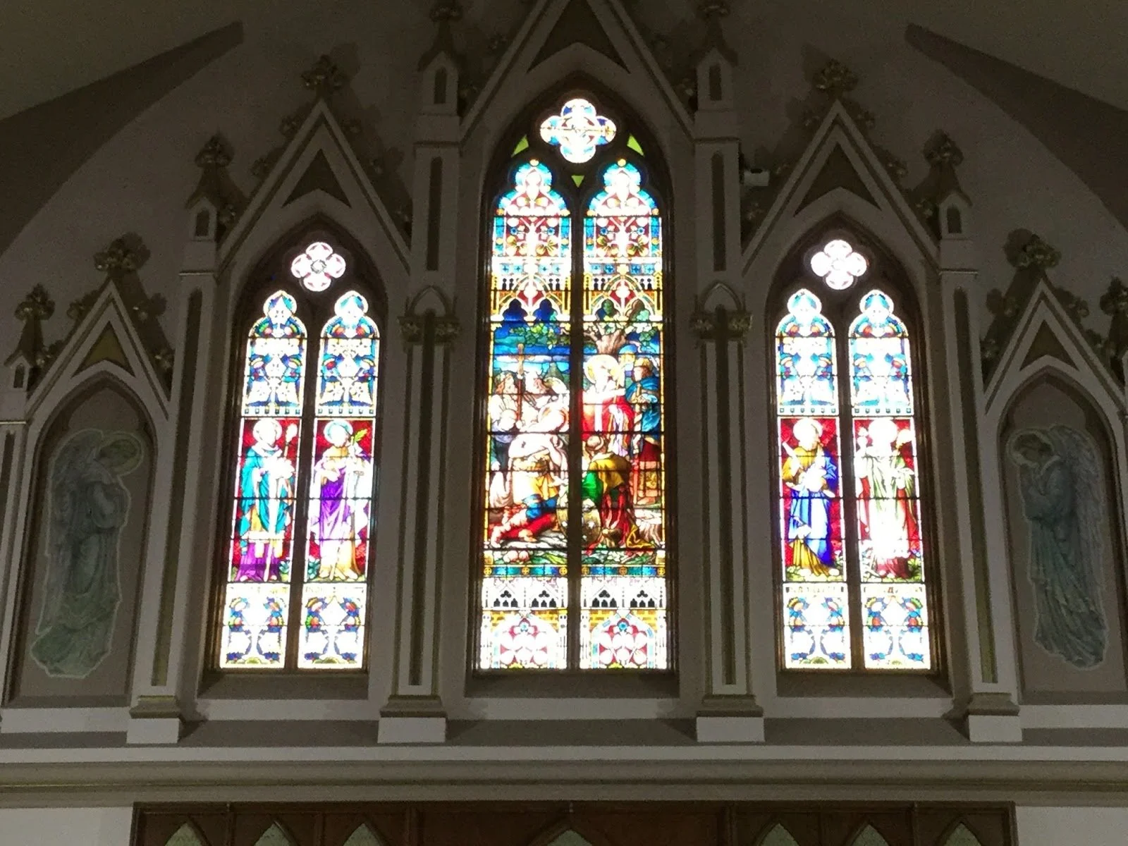 Colorful stained glass windows depicting religious scenes inside a church, with intricate trim and decorations surrounding the windows.