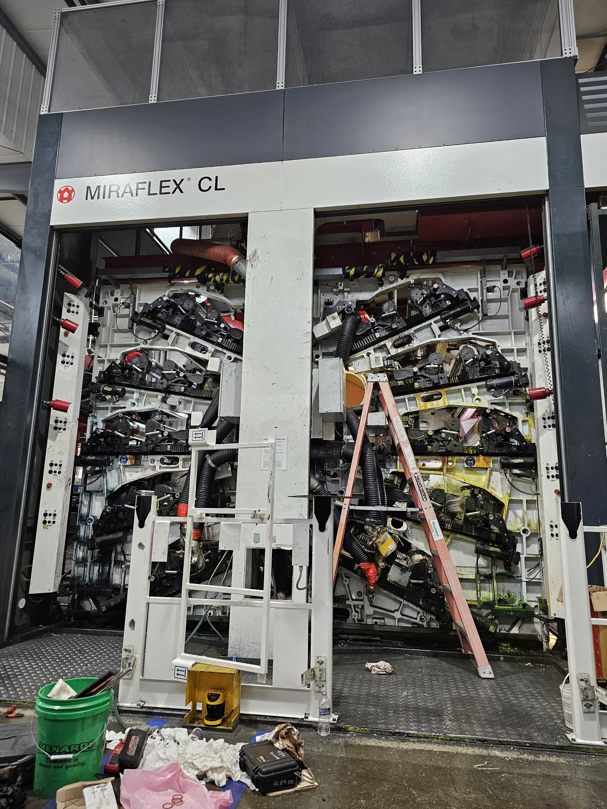 Close-up of a large, industrial machine' with various parts visible and some tools on the floor in front.