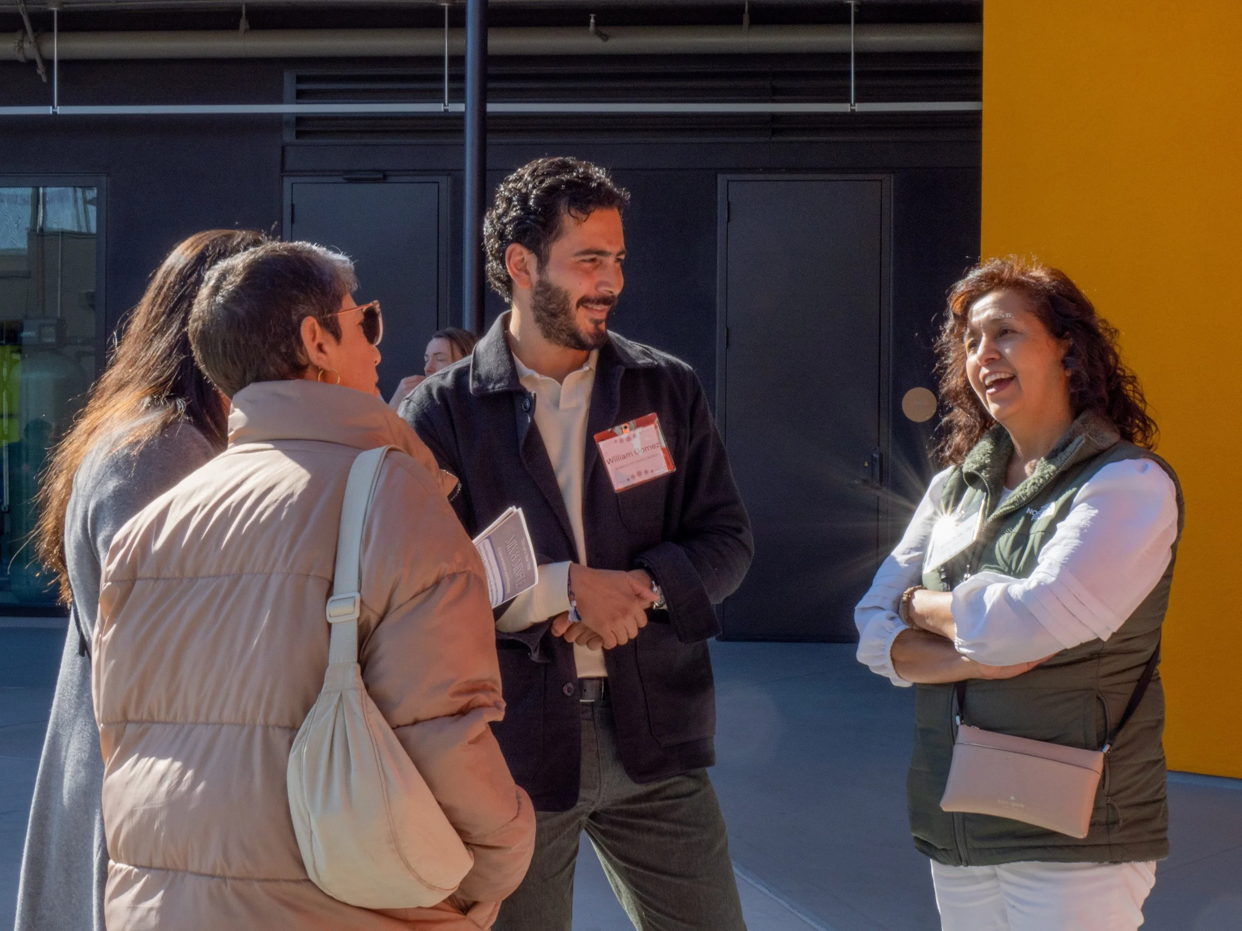 Four people engaged in a conversation outside, with a modern building background. They are smiling and appear to be enjoying their discussion.
