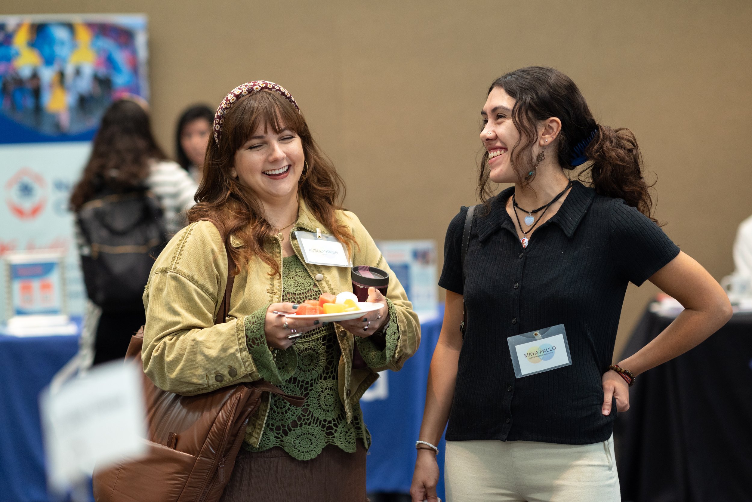 Two women smiling and chatting at a conference or networking event, one holding a plate of food.
