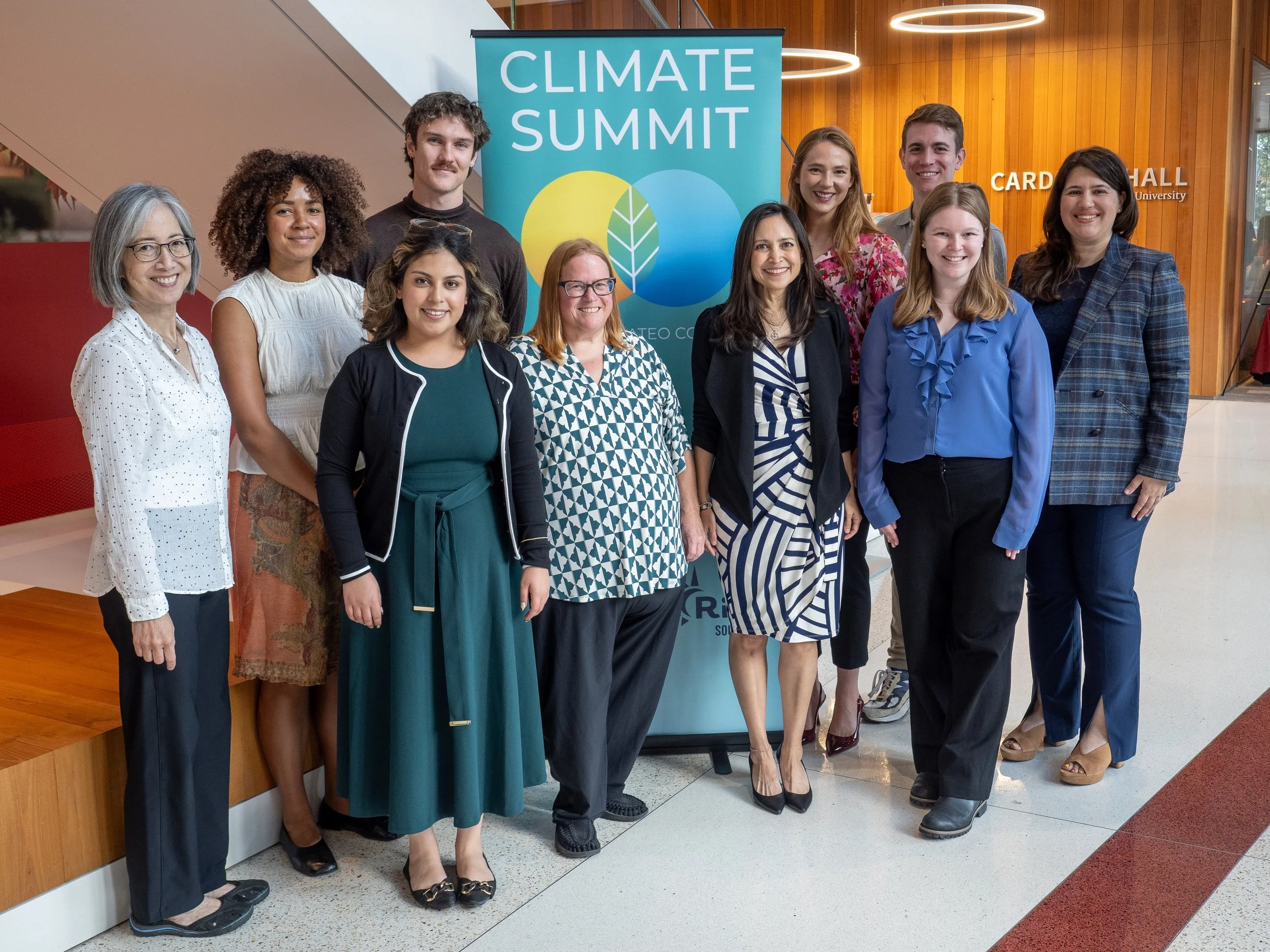 Group of people standing in front of a climate summit banner, posing for a photo inside a modern building with wooden walls.