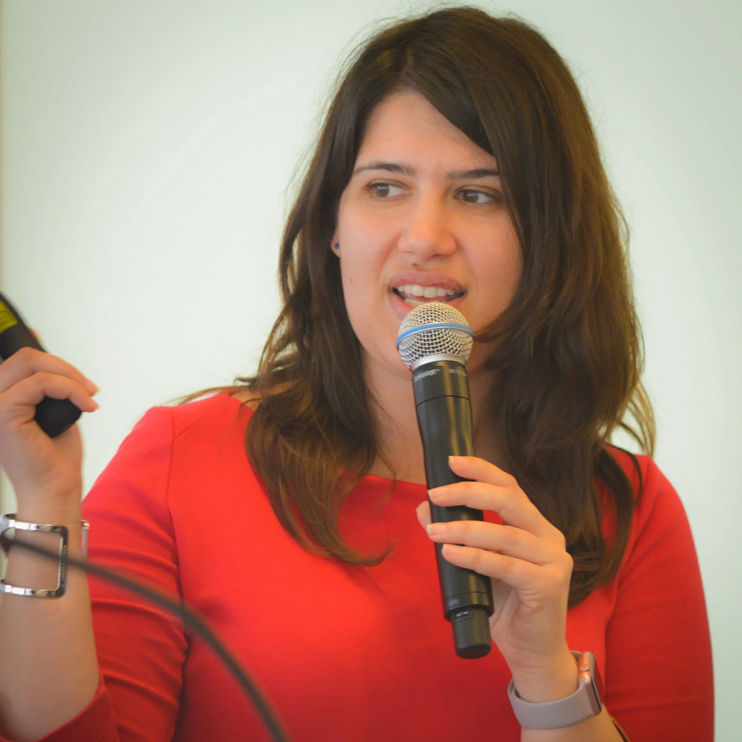 Woman with brown hair in a red shirt speaking into a microphone during a presentation.