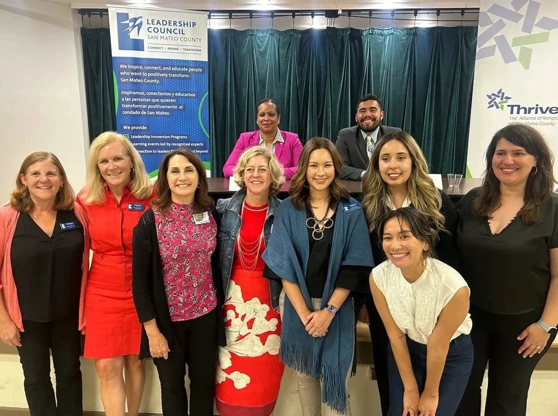 Group of nine people posing for a photo in front of banners at a Leadership Council event in San Mateo County.