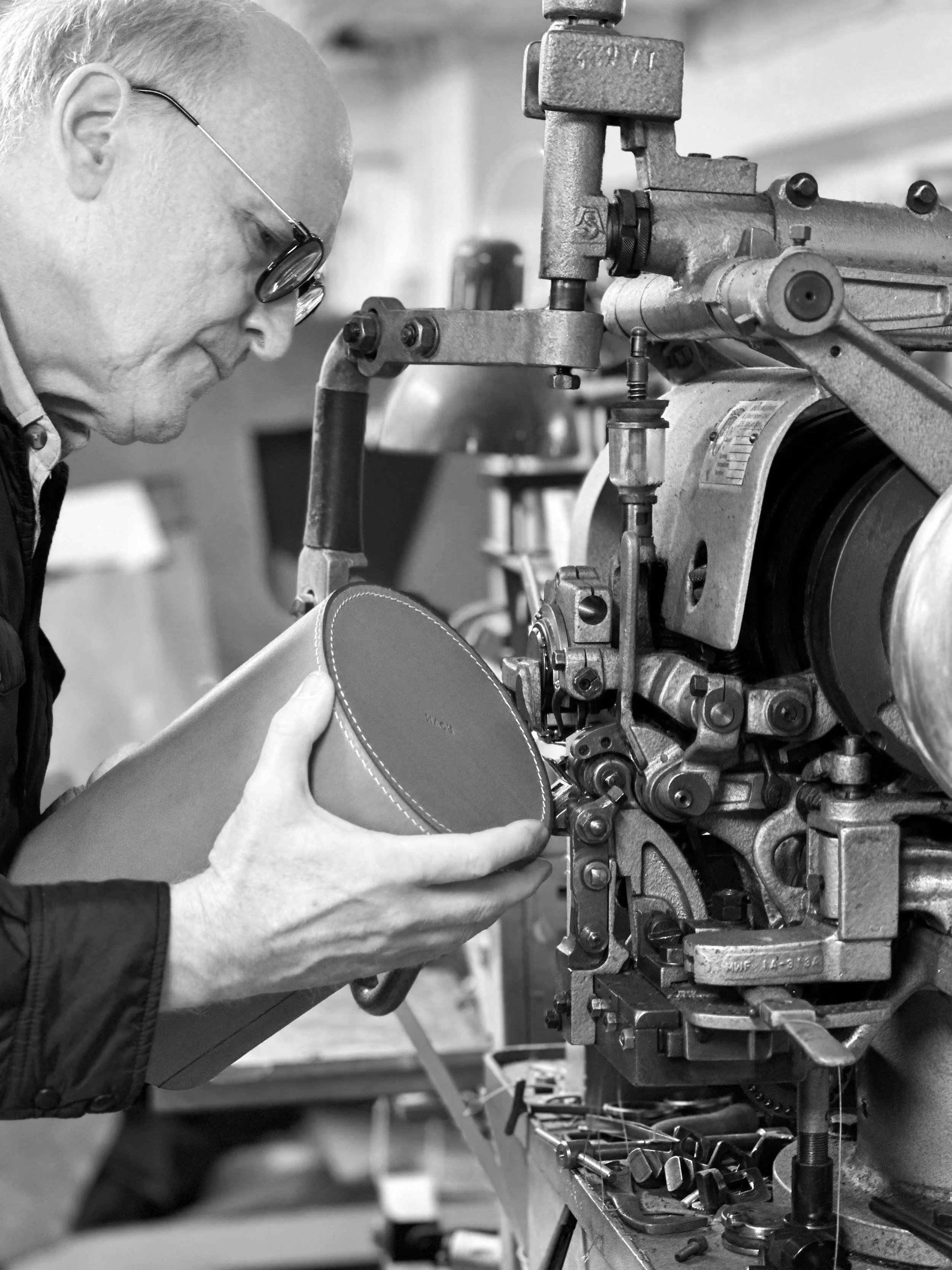 A craftsman stitching an urn with an old edge stitch sewing machine in a small factory setting.