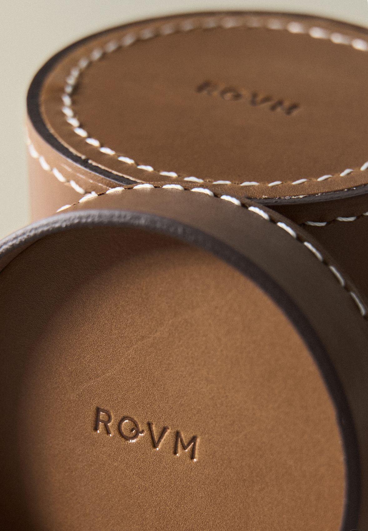 Close-up of a brown leather circular container with white stitching around the edge, and the ROVM brand embossed inside.