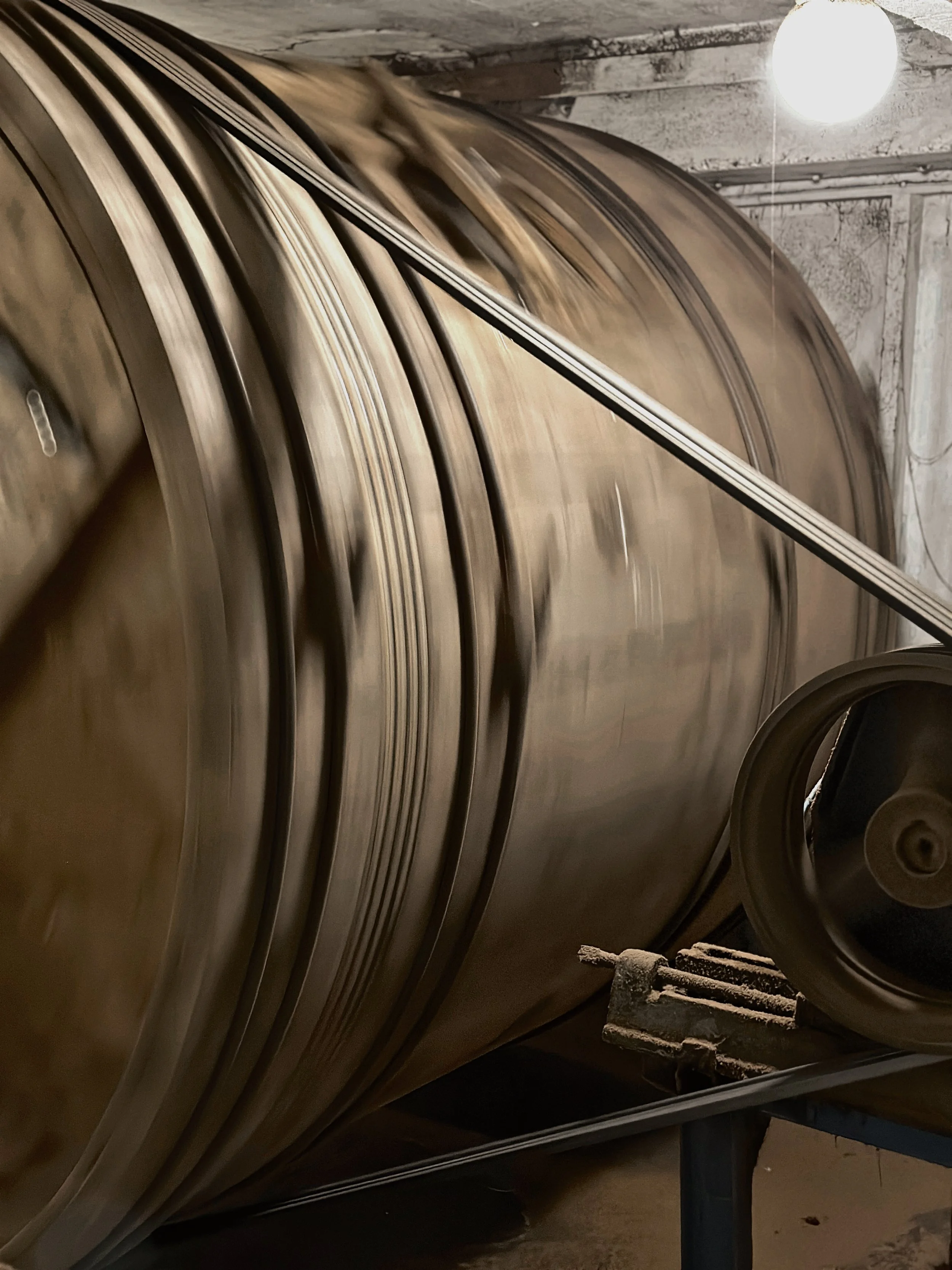 Close-up of large, shiny metal reels or spools stacked on a cart or stand in an industrial setting, with a bright overhead light in the background.
