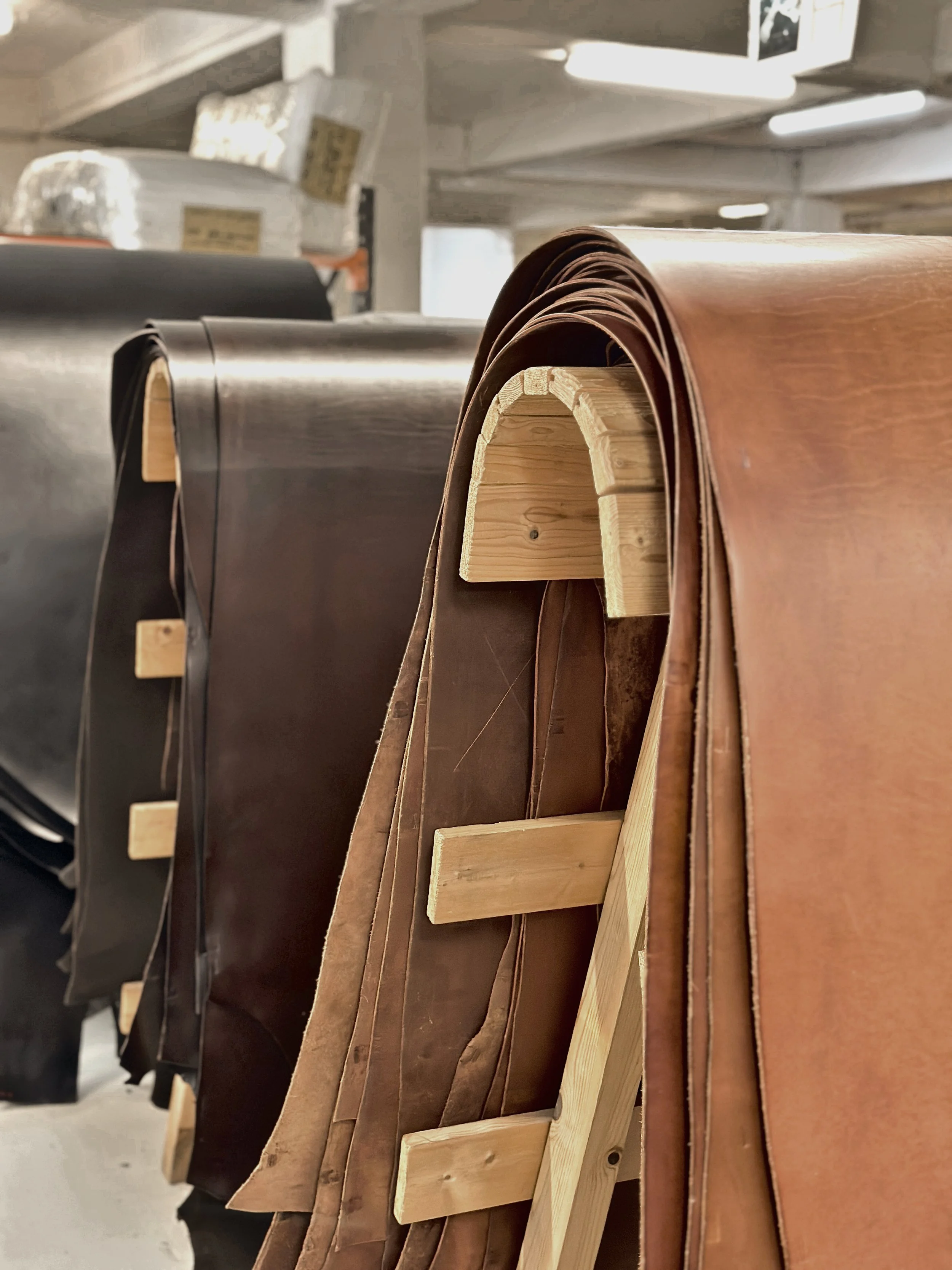 Rolls of different colored leather or fabric materials stacked on a wooden shelf in a warehouse or store.