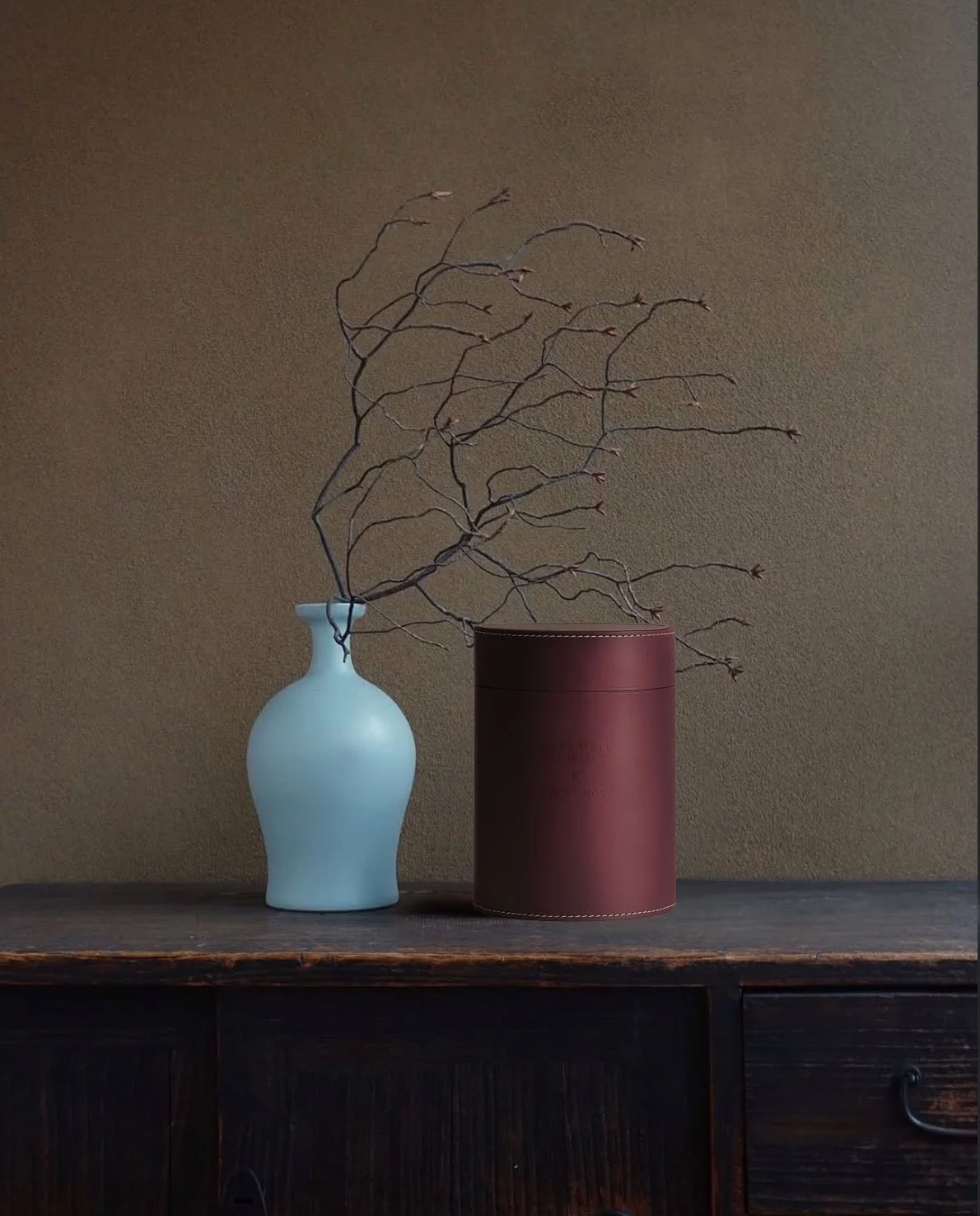 A deep red urn standing next to a plant on a cupboard