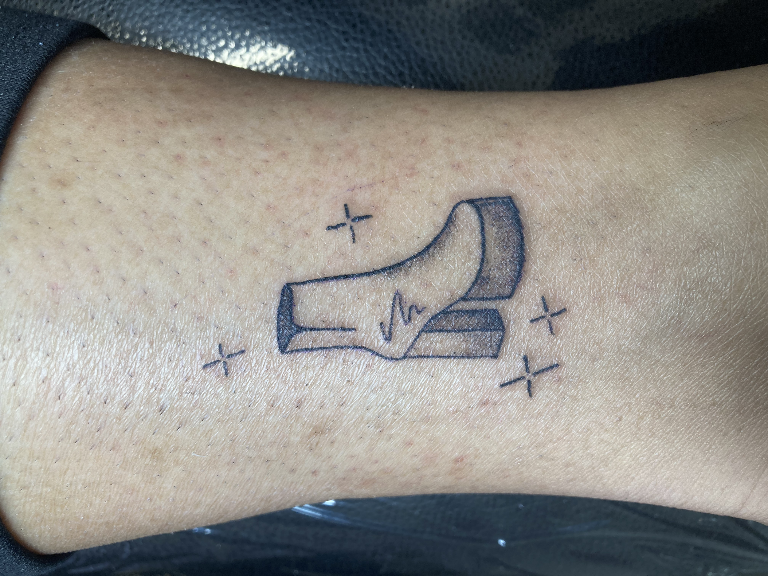 Tattoo of a high heel shoe with a zigzag detail and sparkles around it on a person's ankle.