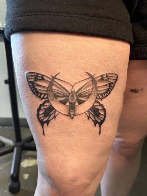 Tattoo of a moth with crescent moon wings on person's thigh