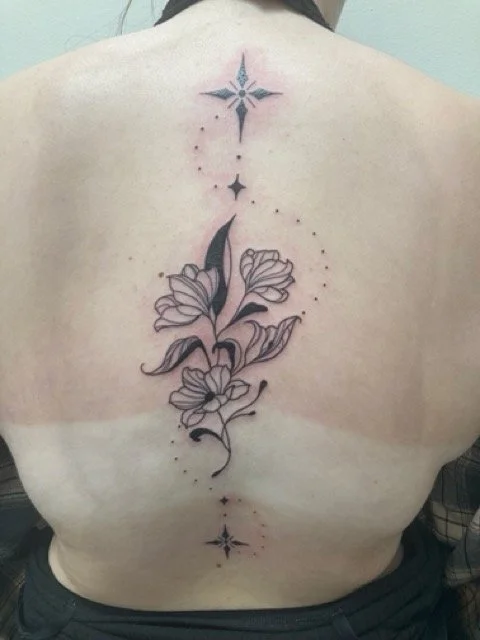 Tattoo of flowers with stars and dots on a person's back. Neotraditional. New-School