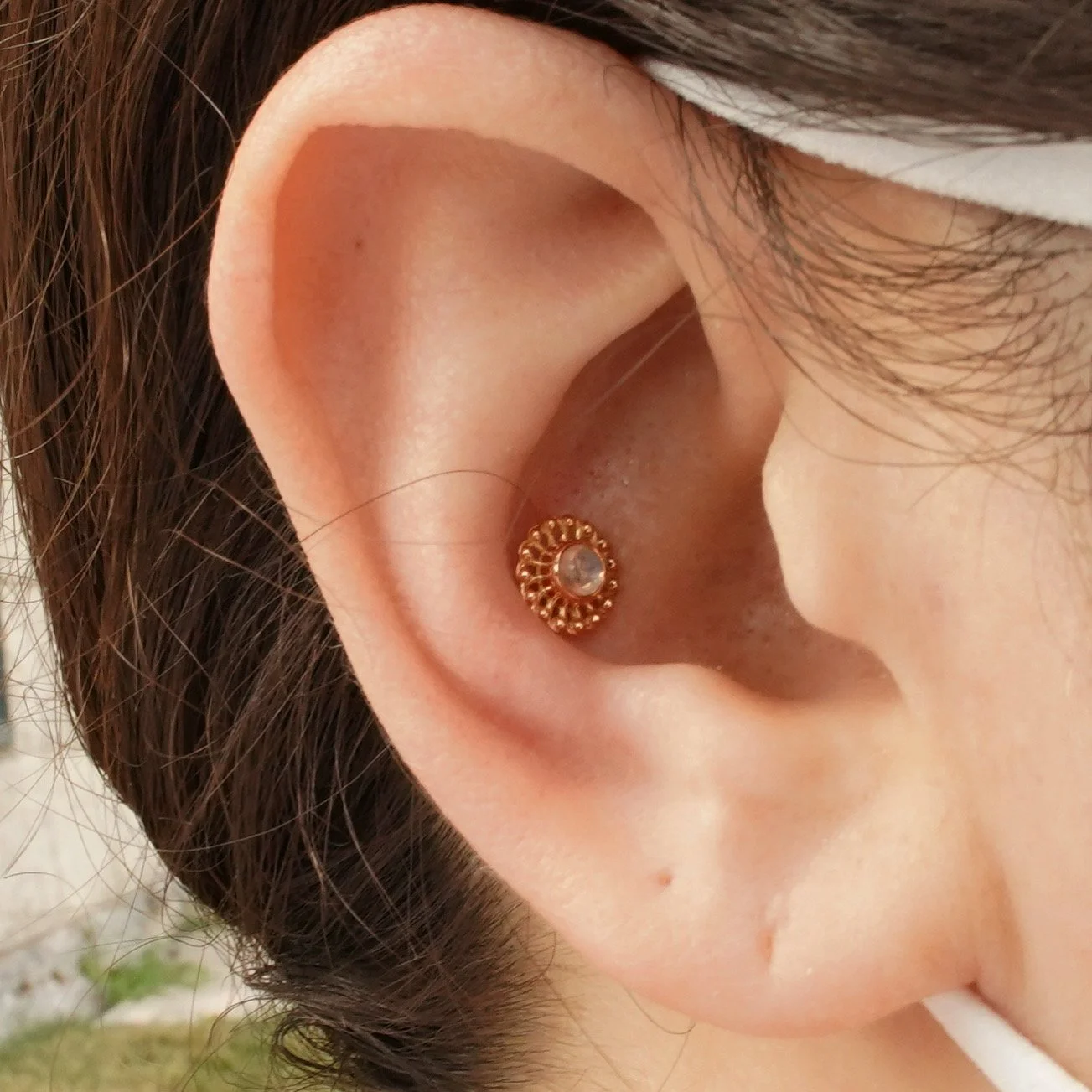 Close-up of a person's ear with a gold earring featuring a small, clear gemstone in the center.