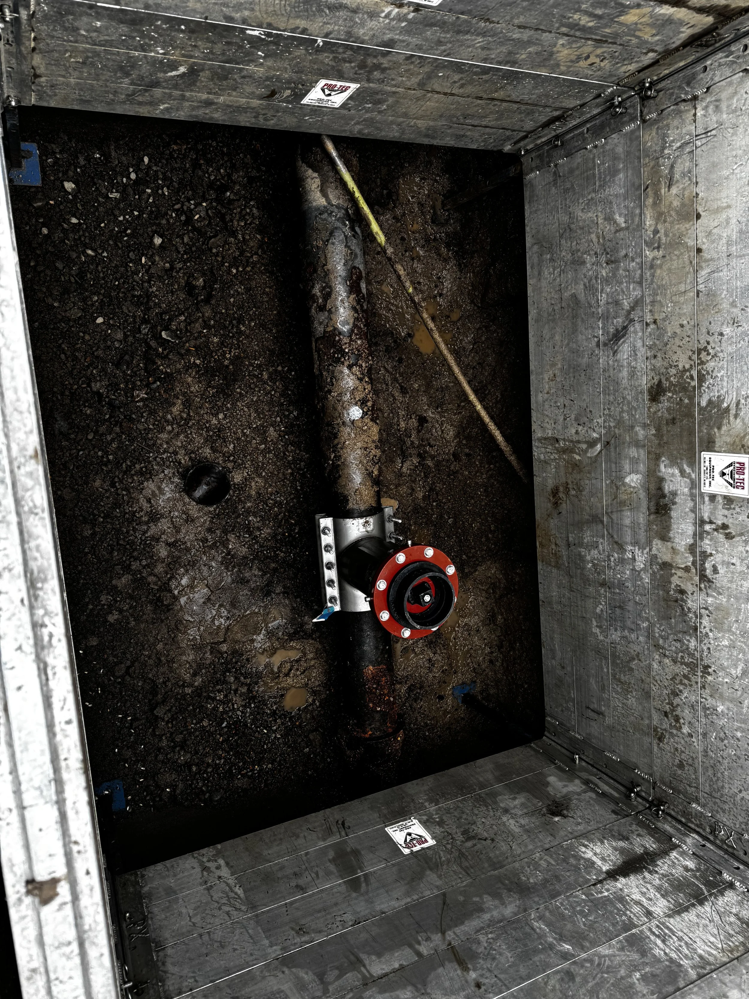 Underground pipe in a metal trench with a valve insertion, surrounded by dirt.