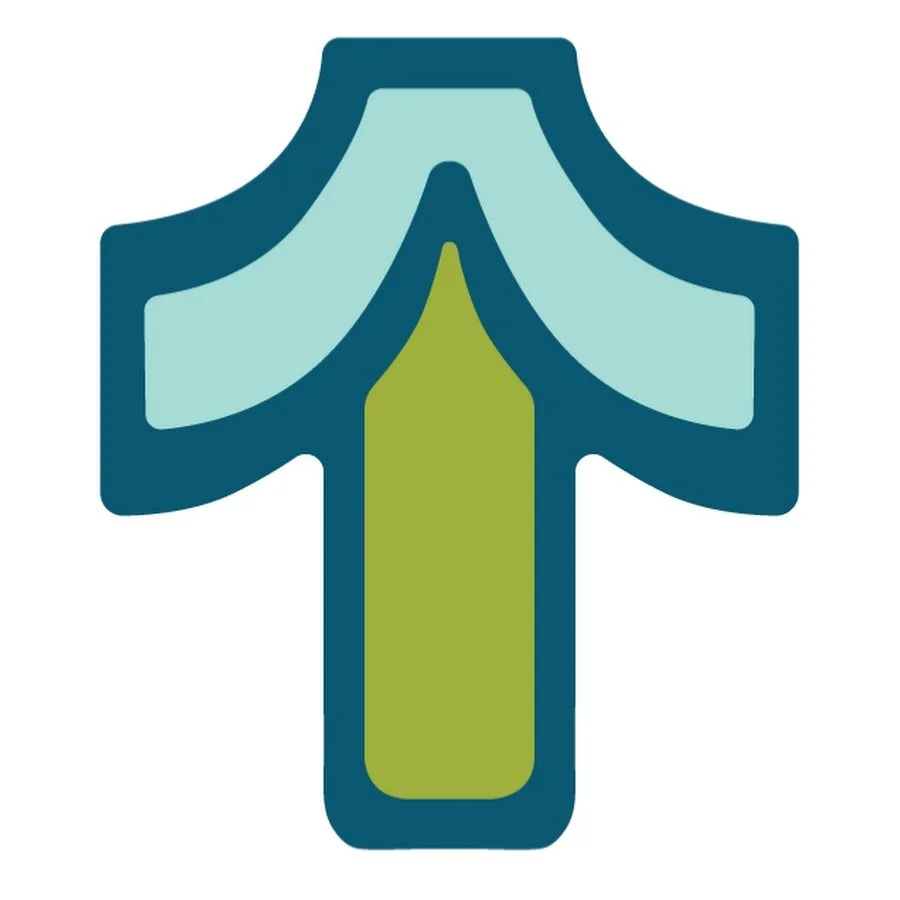 A man with dark curly hair, glasses, and a mustache and beard, wearing a dark sweater, smiling softly indoors with a blurred background, including a plant.