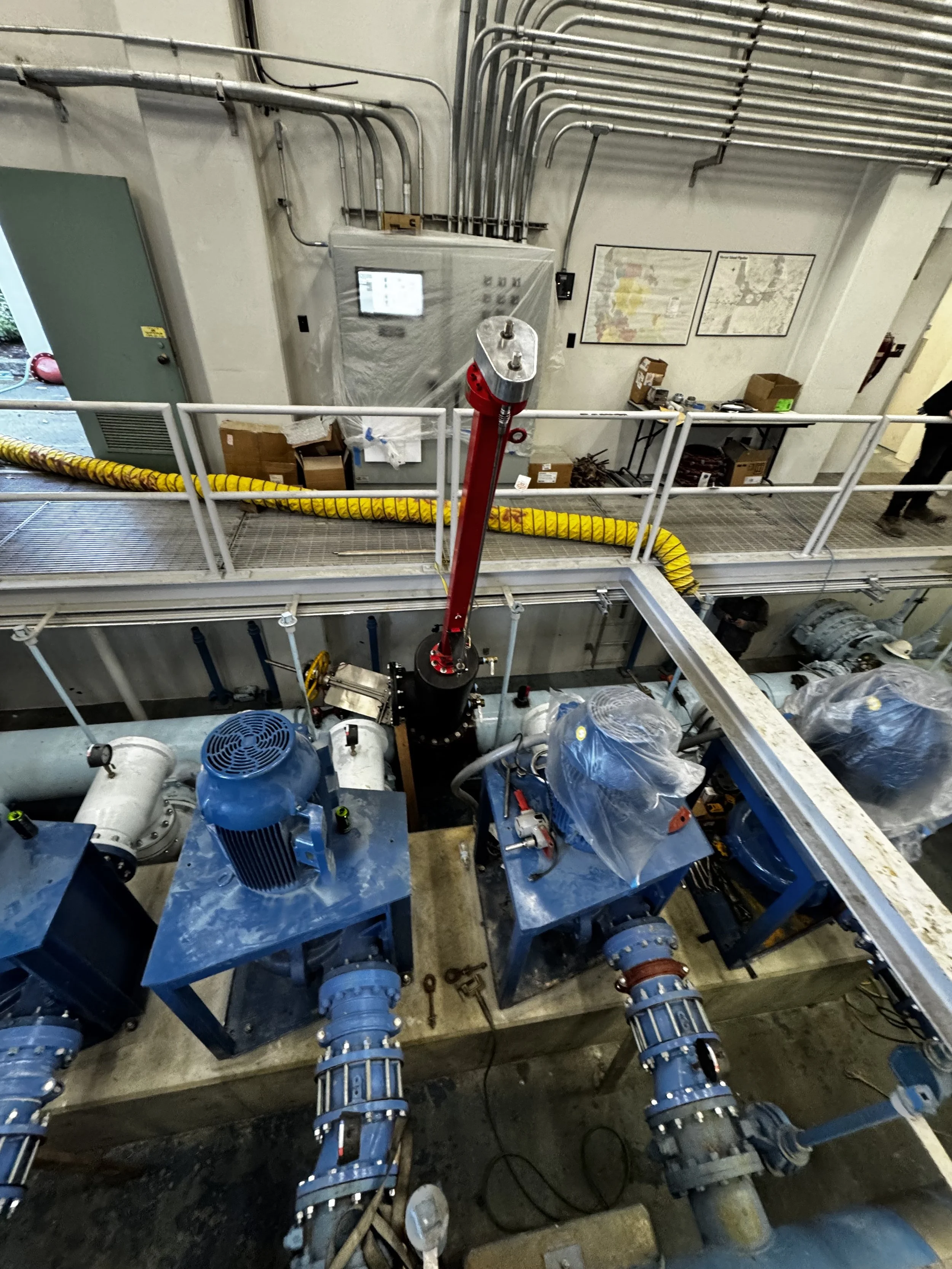 Industrial machinery with blue motors and pipes in a factory setting, with a monitored control panel and work platform above.