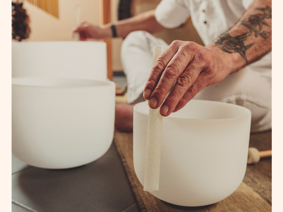 Person playing crystal singing bowls, rubbing a mallet on the rim of a white singing bowl.