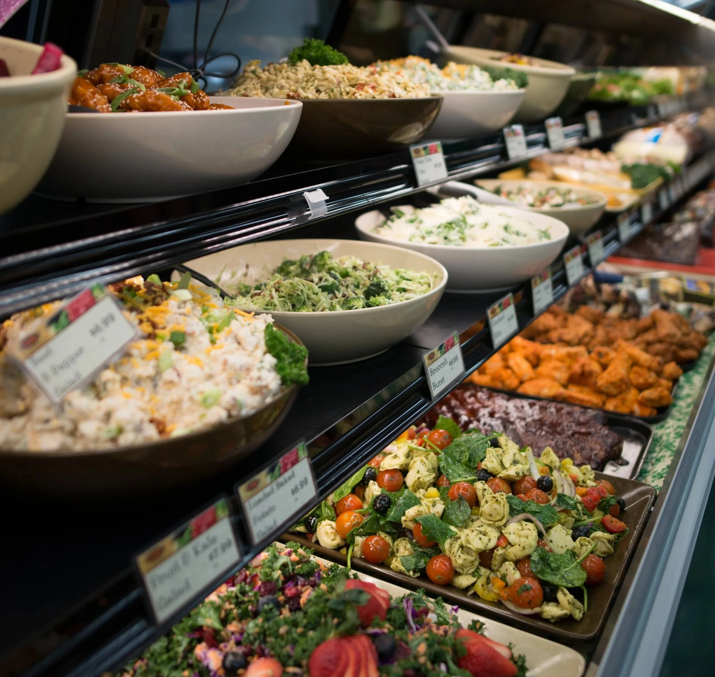 Assorted deli meats, cheeses, salads, and prepared foods displayed in a grocery store deli case.