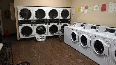 A laundromat with stacked washers and dryers along the wall and washing machines on the right side.