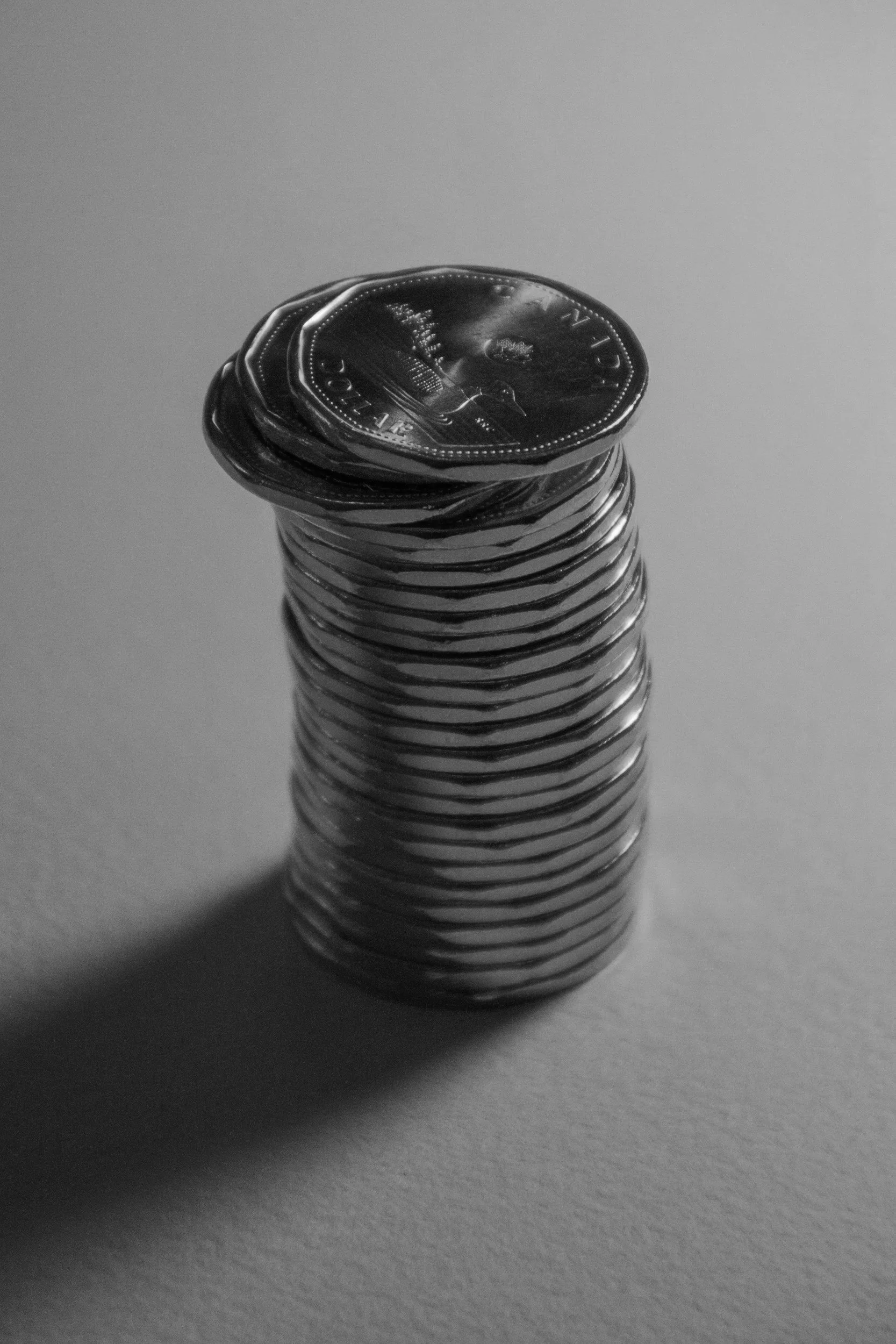 Stack of coins with some on top, casting a shadow on a plain surface.
