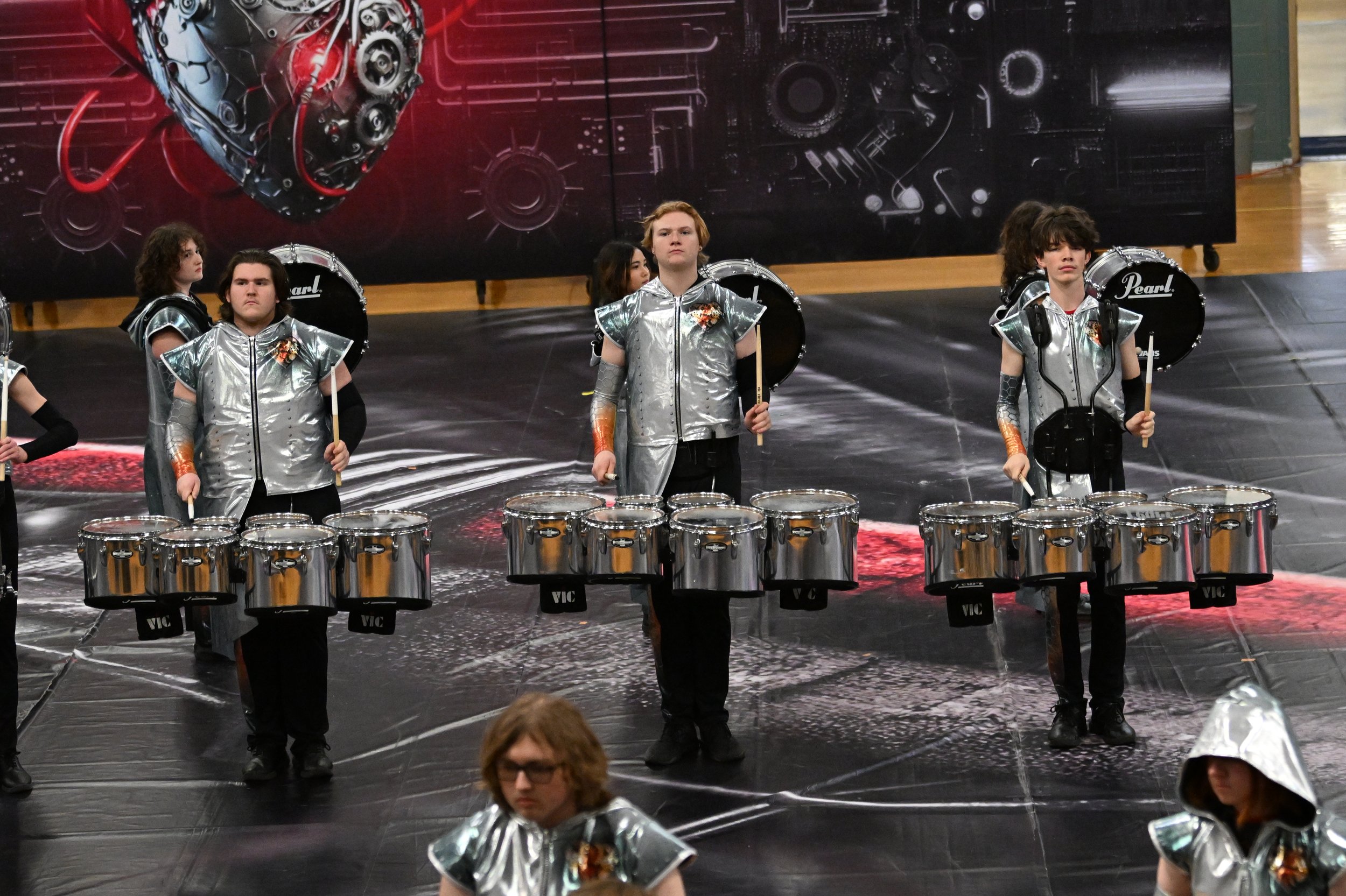 Children in silver costumes performing with steel drums on stage during a group event.