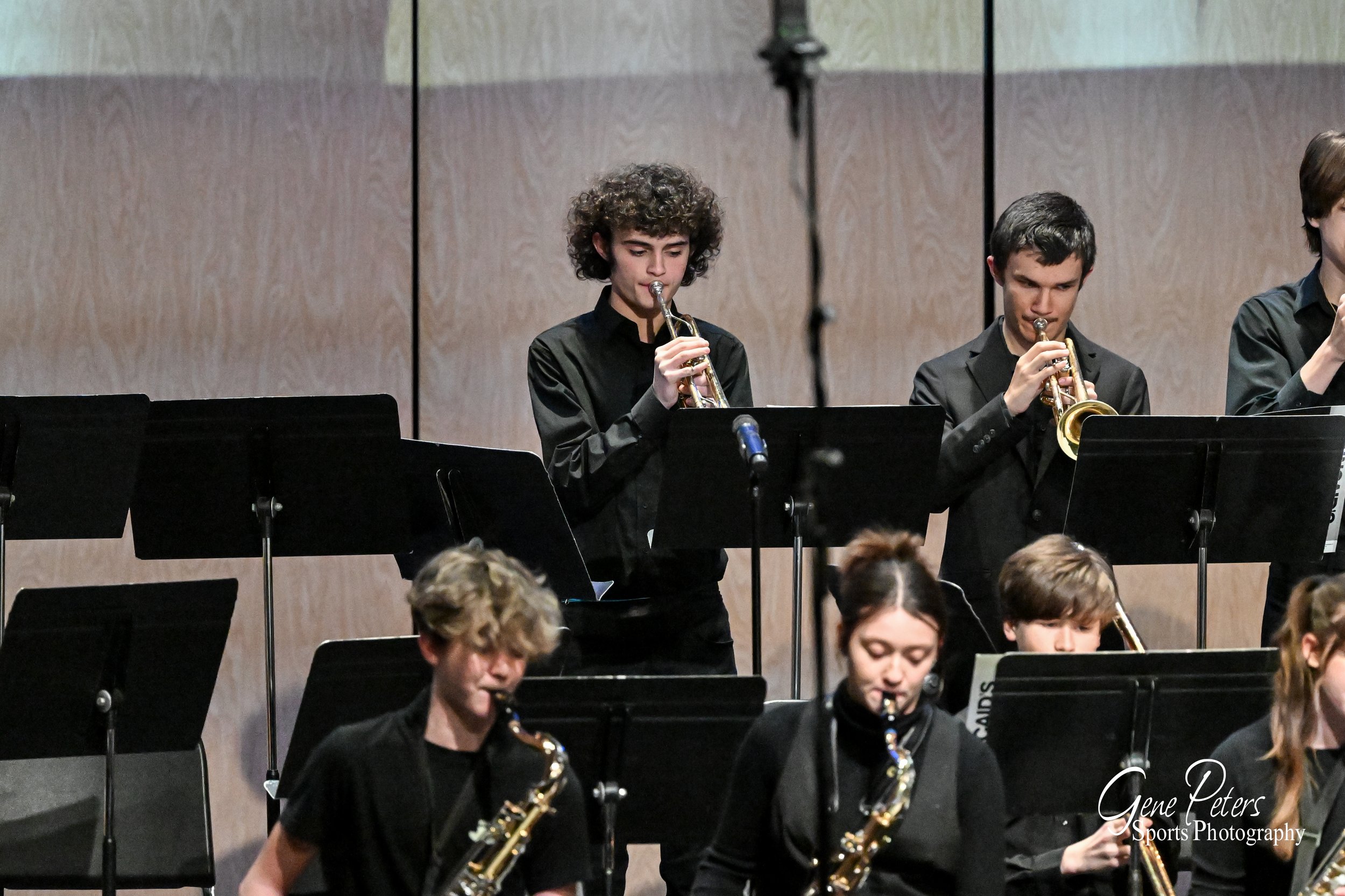 Young musicians in black outfits playing wind instruments in a concert hall.