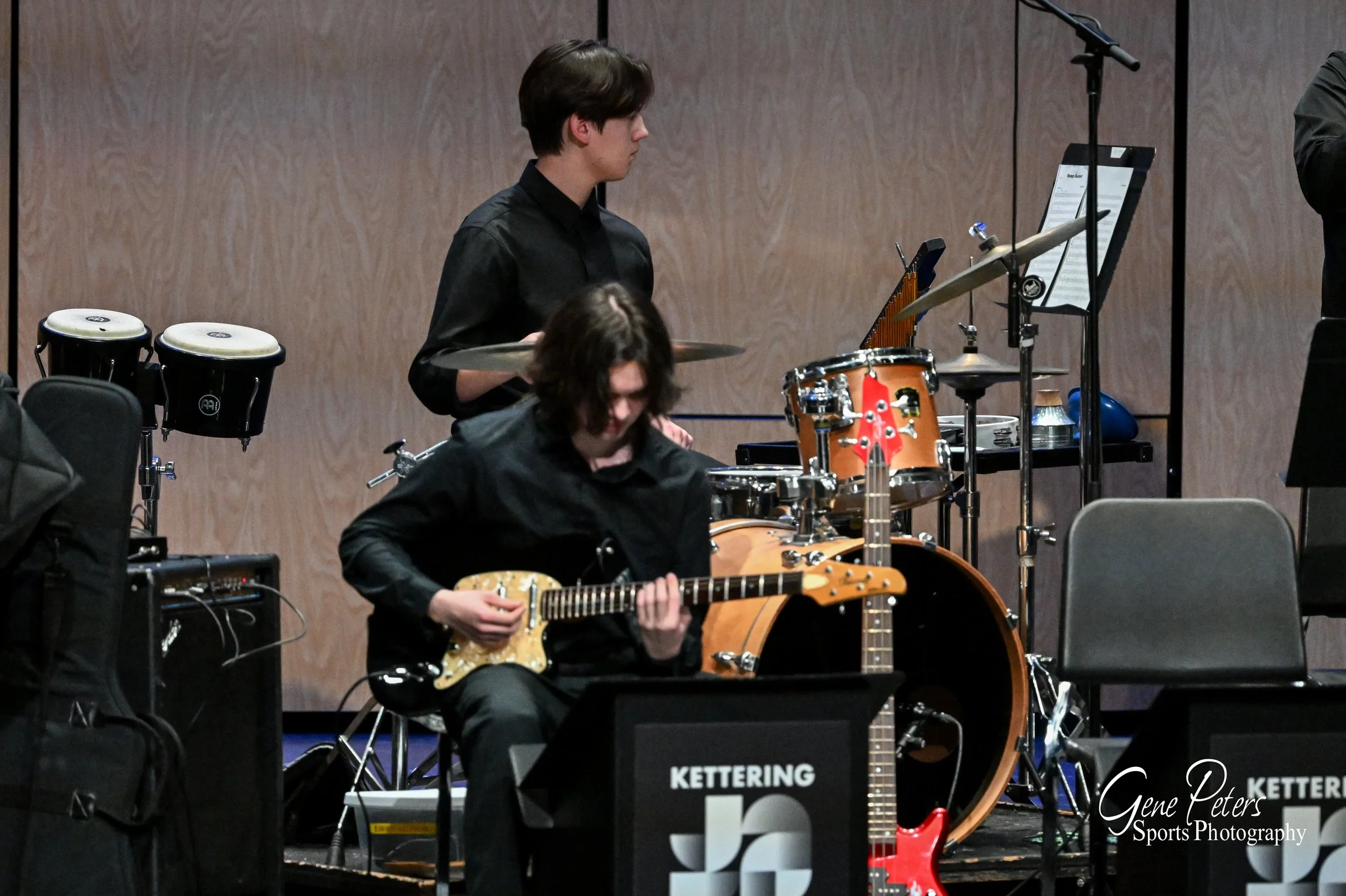 Musicians performing on stage at Kettering event, with one person playing guitar and another on drums.