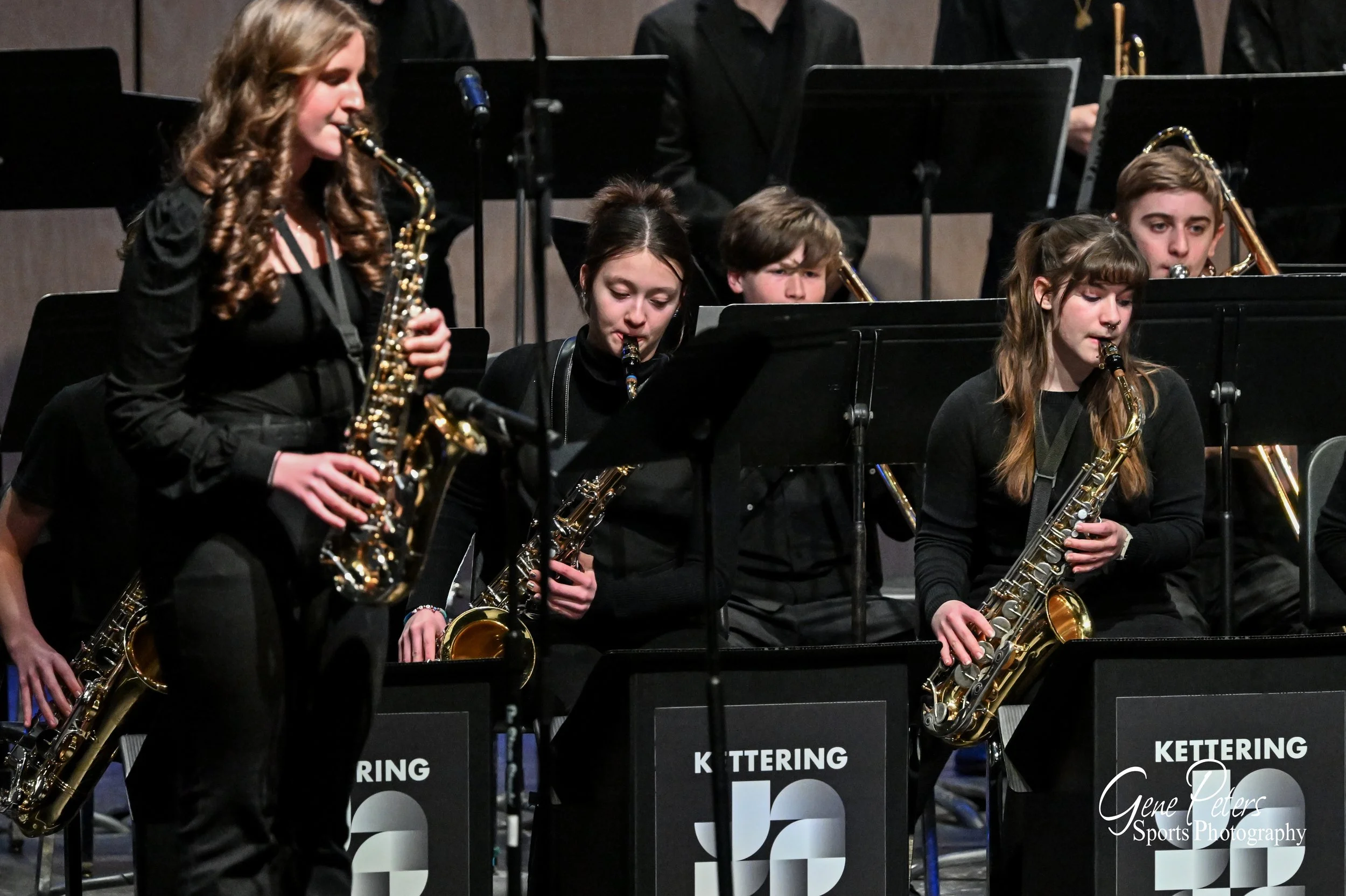 A group of young musicians playing saxophones during a concert, with music stands labeled 'Kettering'.