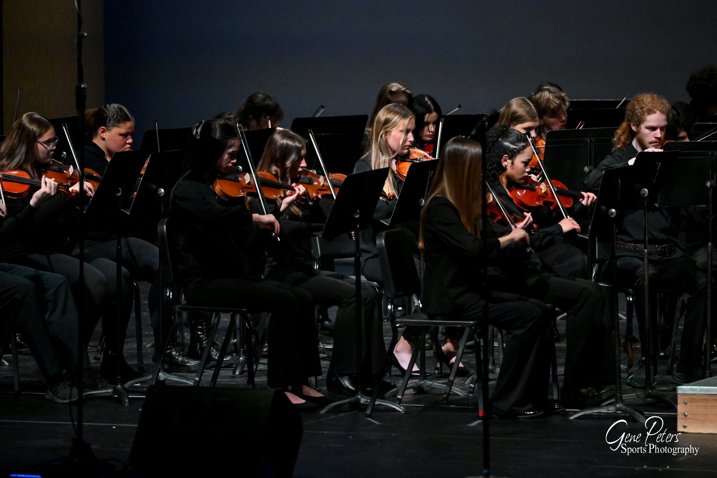 Orchestra with young musicians playing violins on stage during a performance.