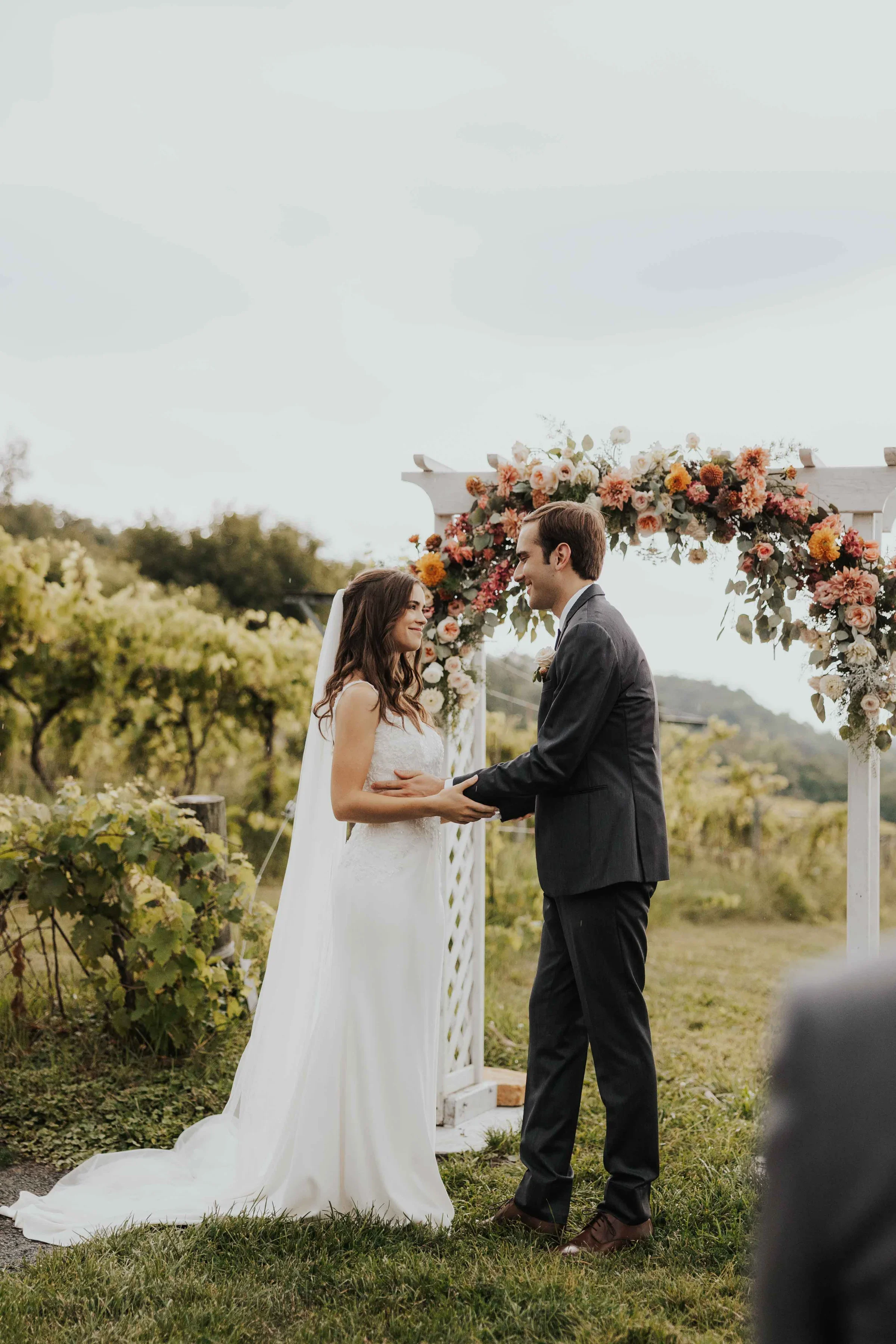 Couple exchanging vows at outdoor wedding ceremony with floral arch.
