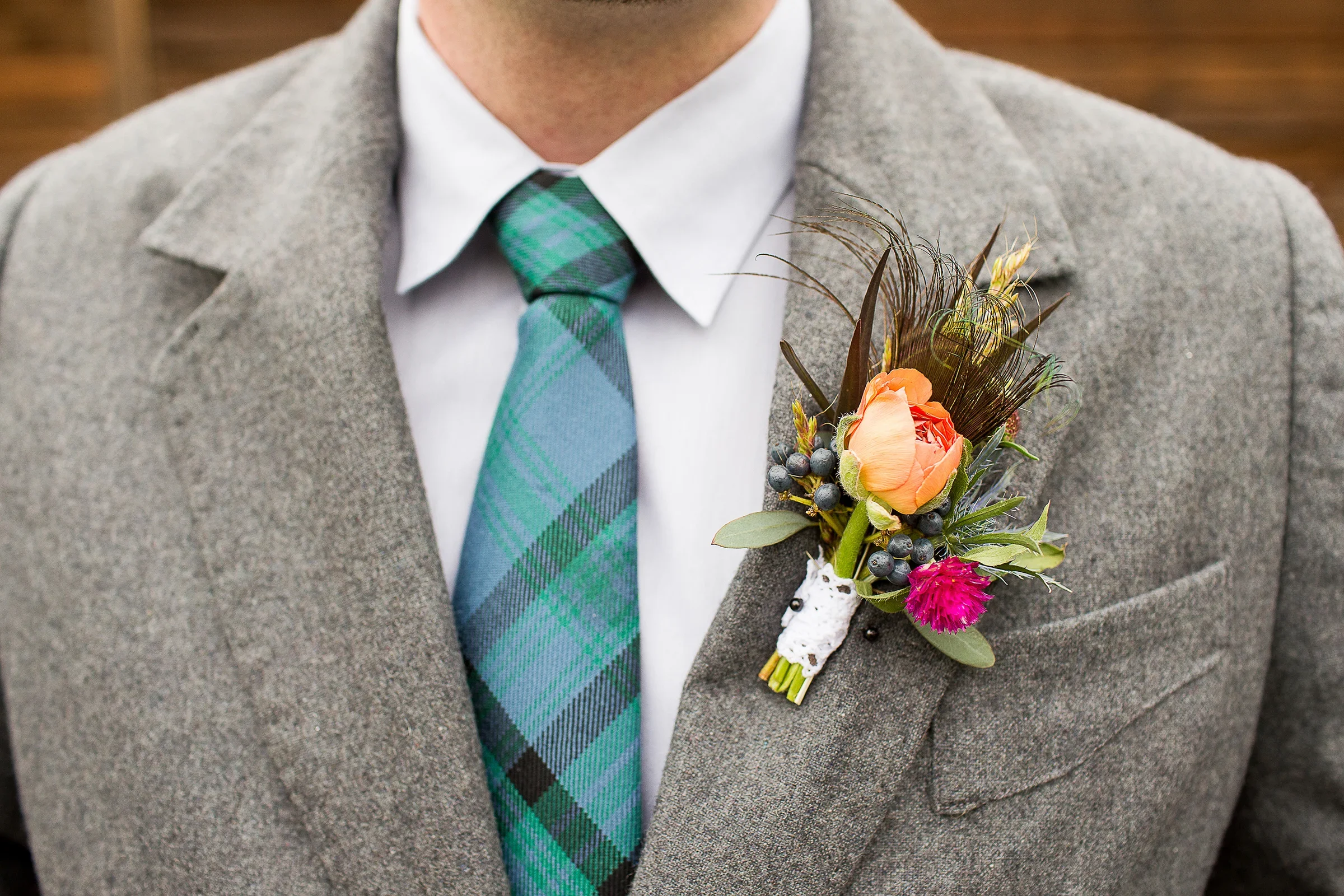 Man wearing a gray suit, white shirt, and a blue-green plaid tie, with an orange rose boutonniere on the lapel.