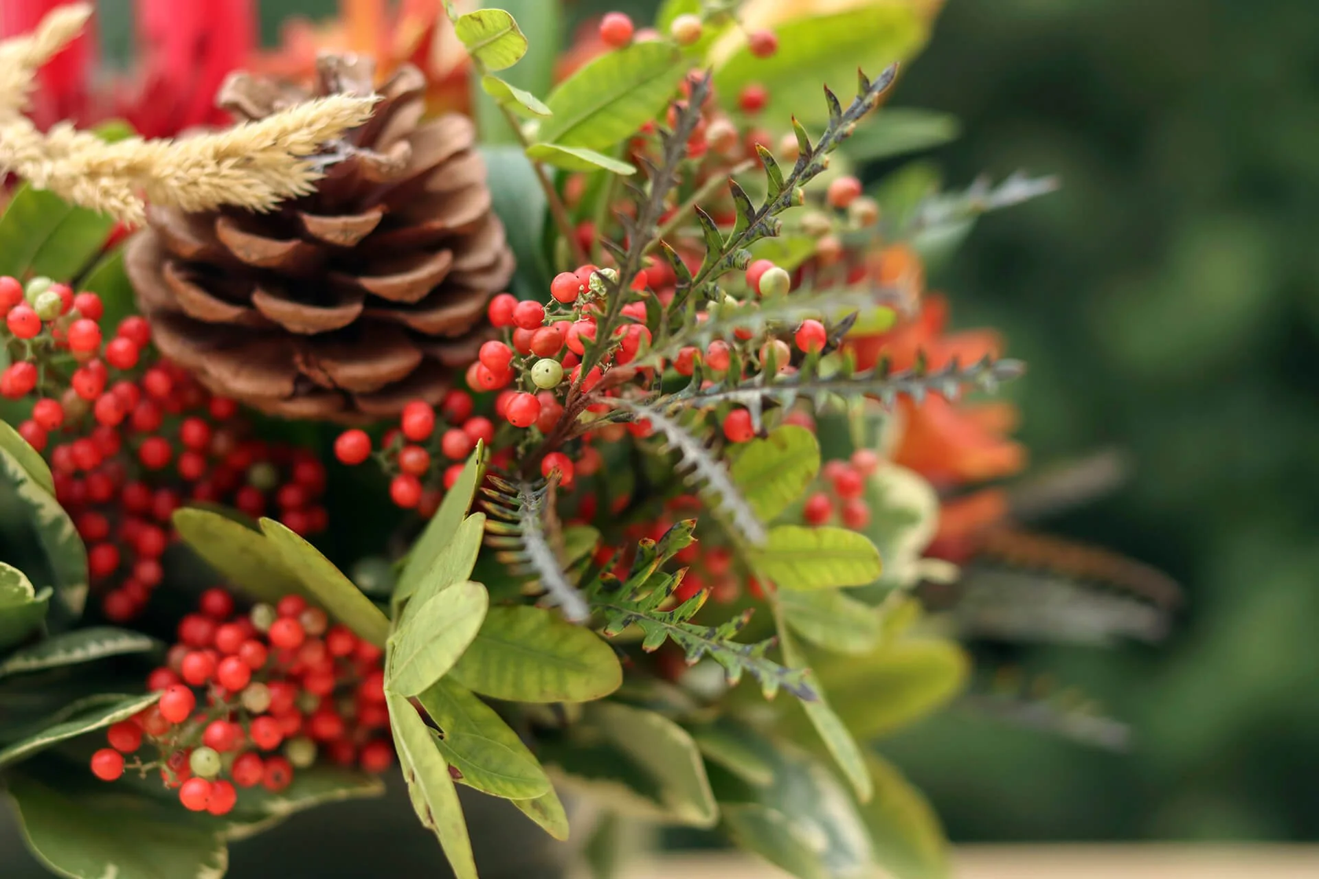 Holiday floral arrangement with red berries, greenery and pine cones.