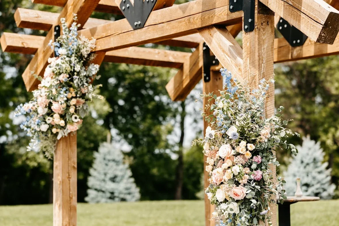 Wooden wedding arch decorated with pastel-colored flowers and greenery in an outdoor setting.