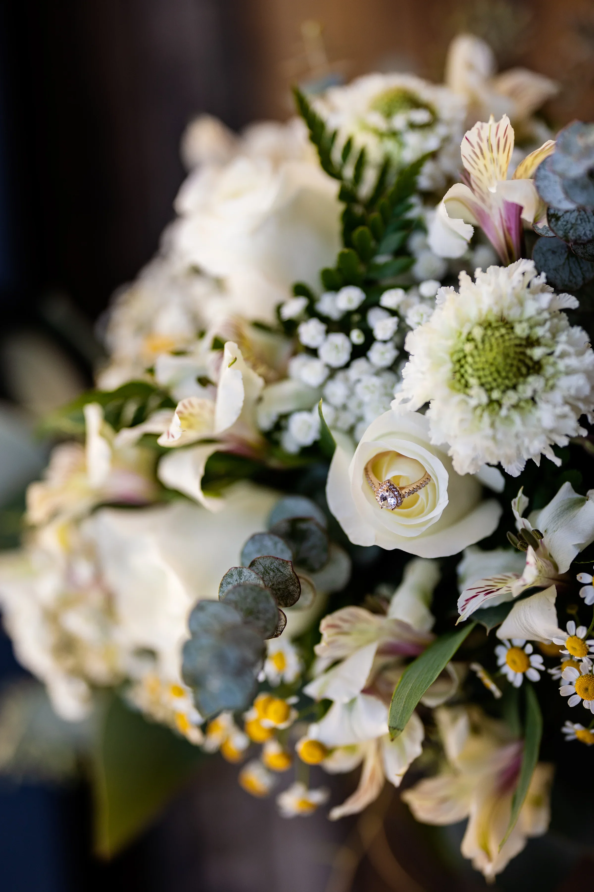 A bouquet of white flowers including roses, daisies, and baby's breath with a diamond ring nestled inside a white rose.