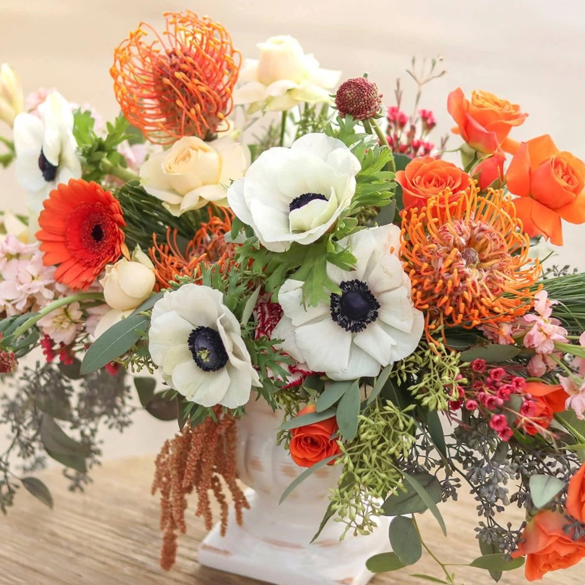 Floral arrangement in a white vase placed on a wood table.