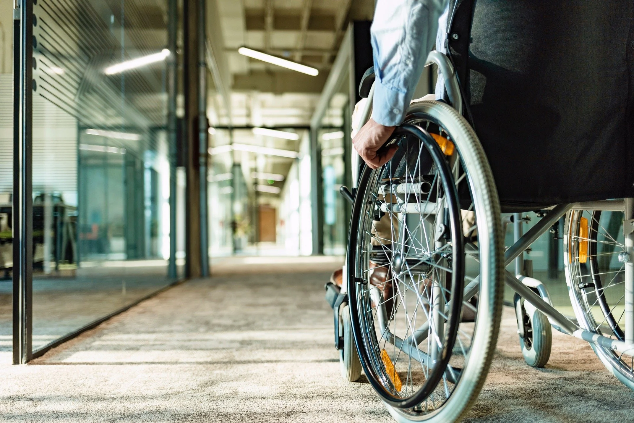 Person in a wheelchair walking through a modern building with glass walls and natural light.