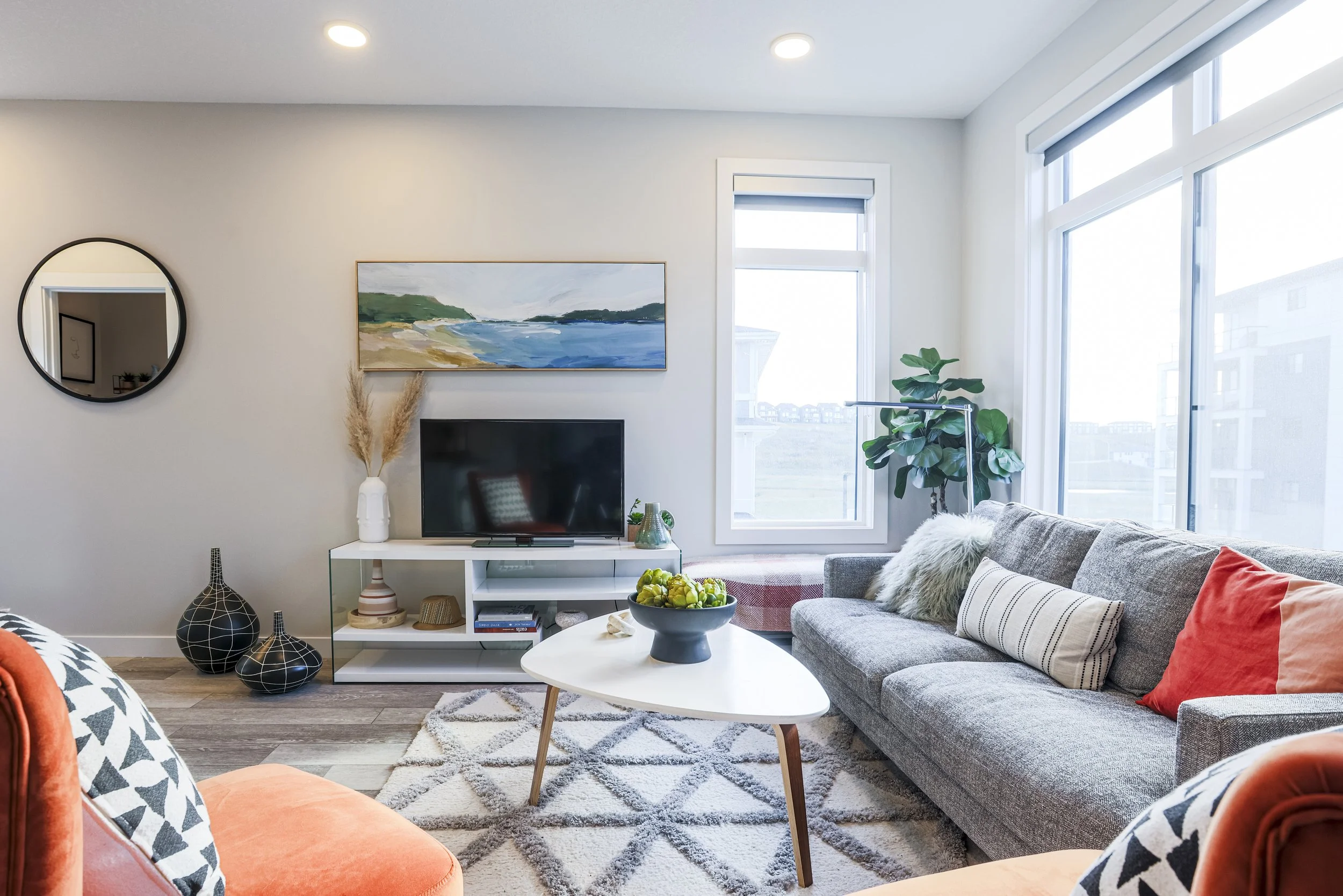 Bright living room with gray sofa, white coffee table with fruit, large windows, and contemporary decor.
