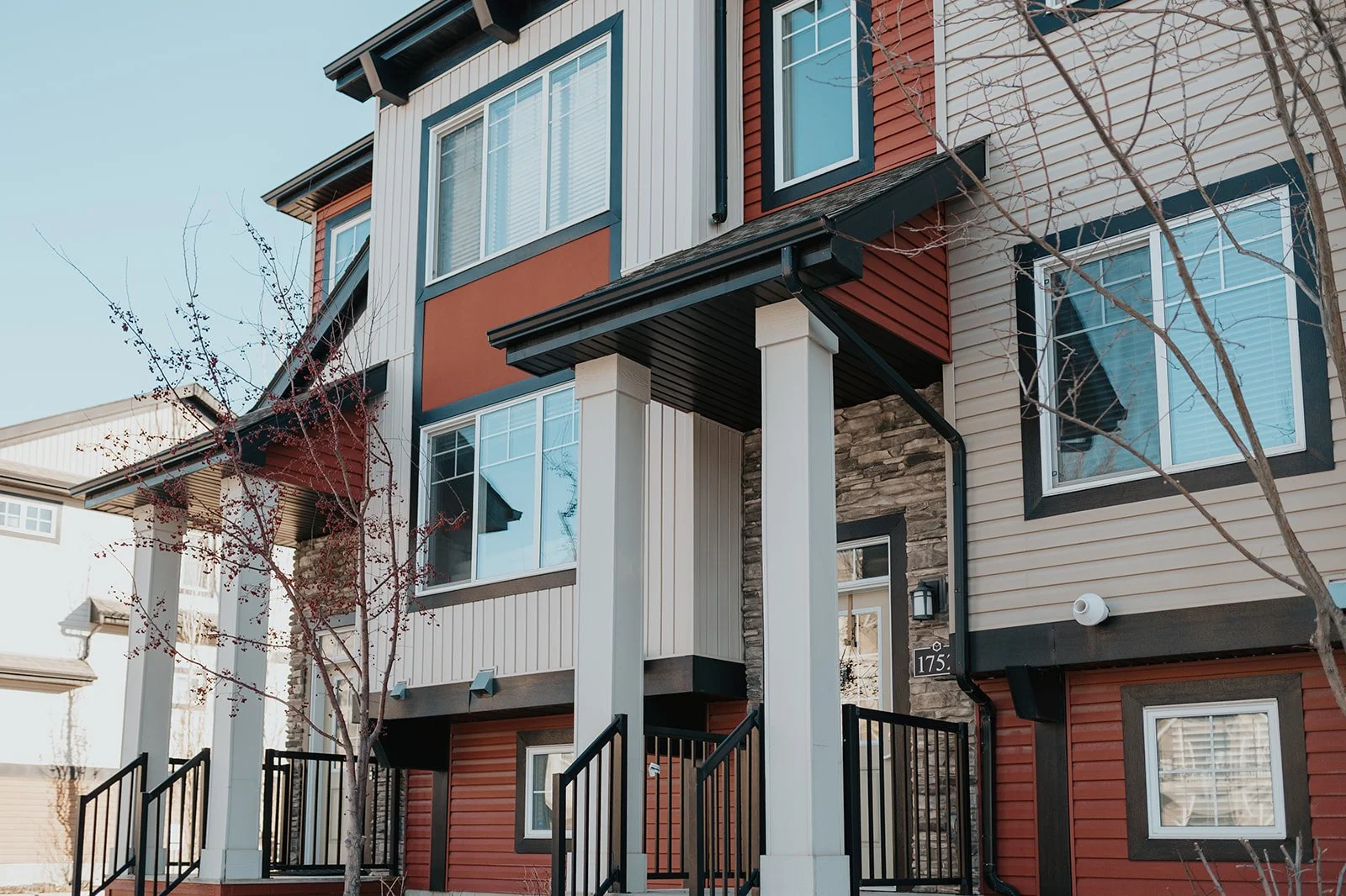 Close-up of a modern multi-story residential building with colorful siding, large windows, and a small front porch with stairs.