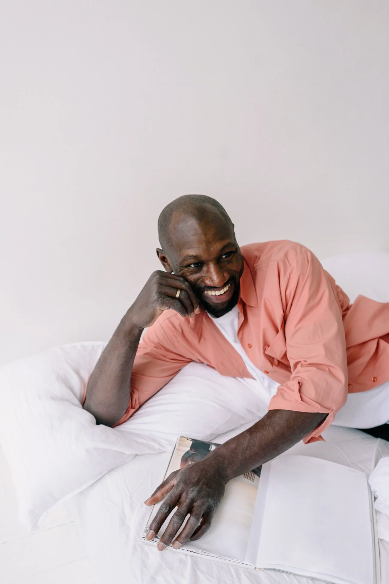 A man with his hand on his face, laying on a white bed.