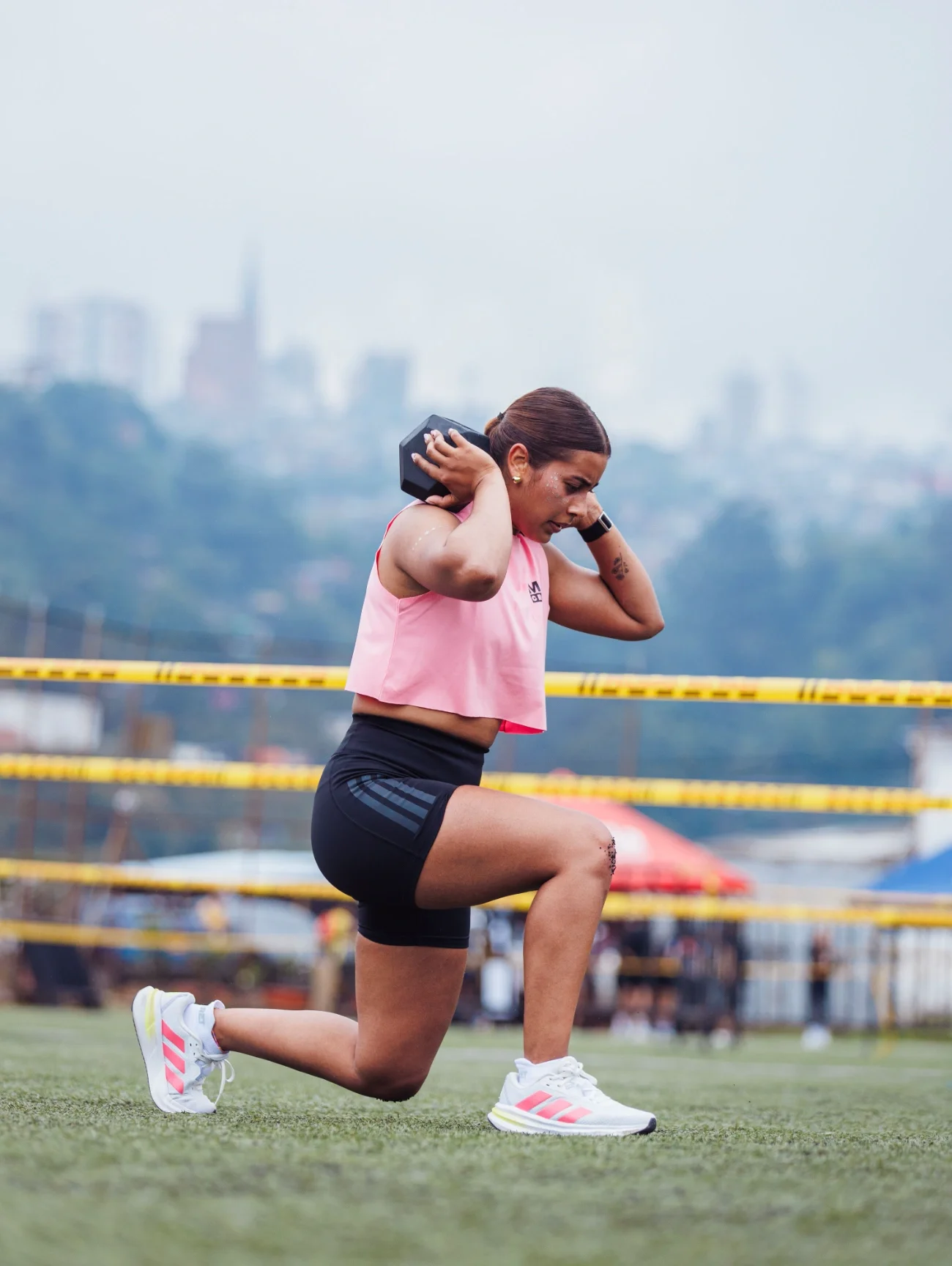 A woman exercising with weights outside with a city skyline behind her.