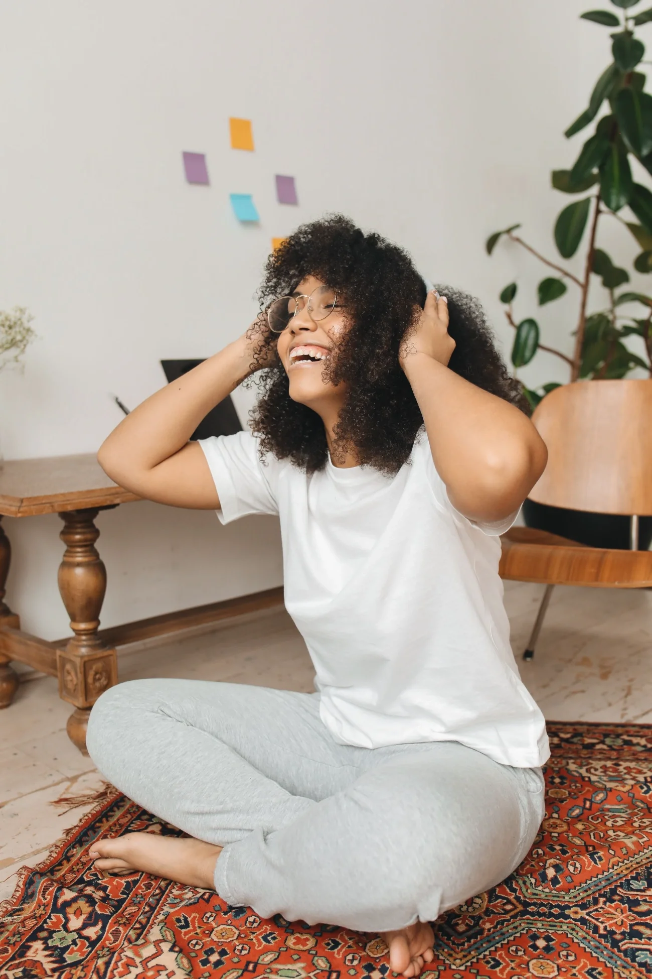 A young woman sitting on a carpet, listening to music through headphones, smiling.