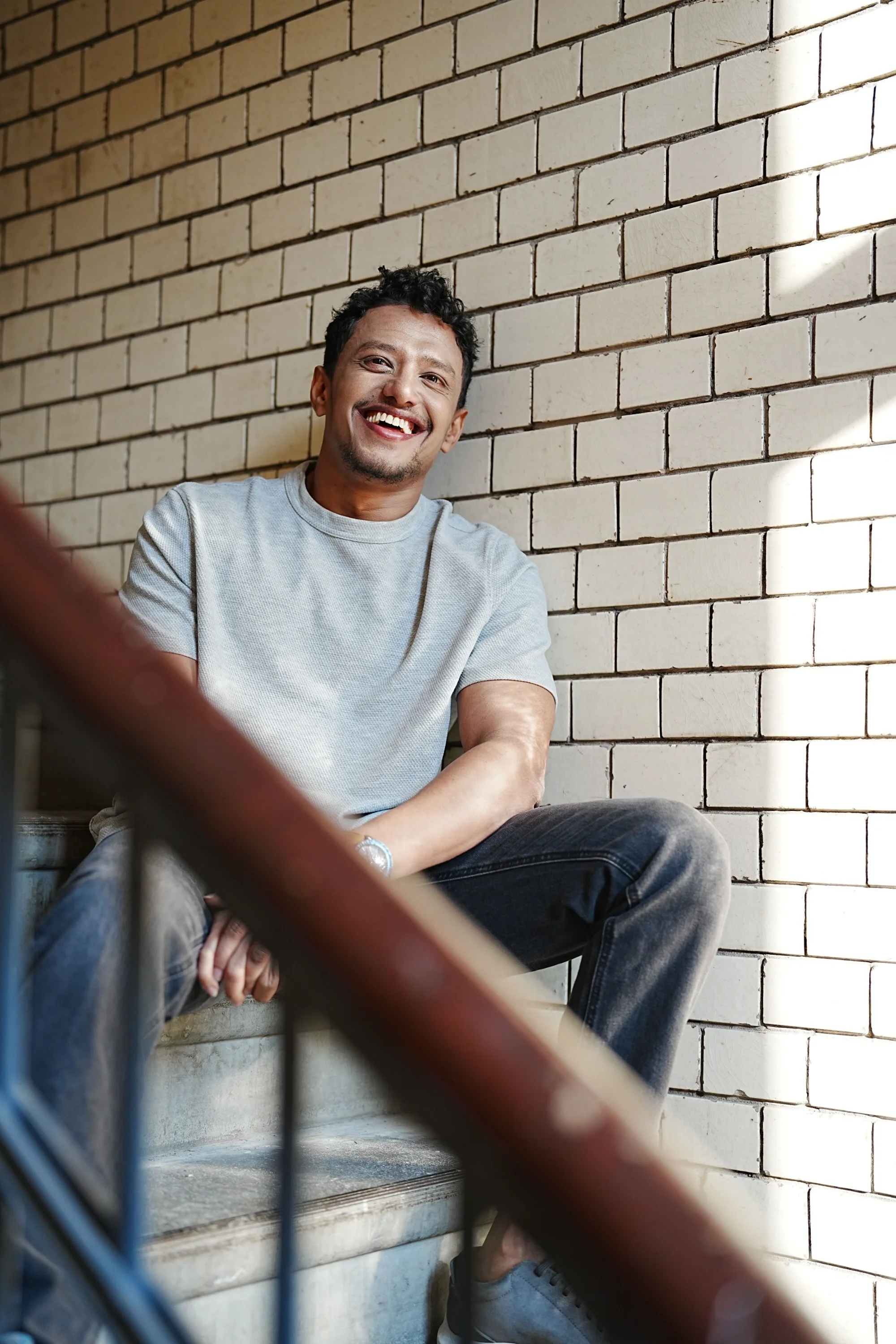 A man sitting in a stairwell, smiling and looking at the camera.