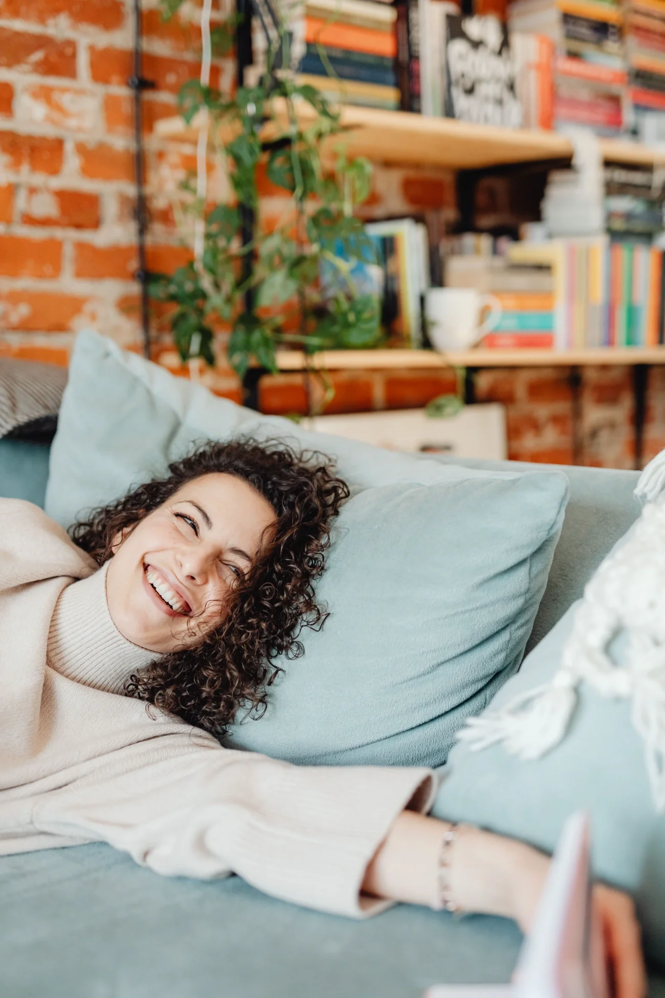 A woman smiling and looking away from the camera, laying in a bed. Noia Wellness Therapy in Hamilton, Ontario