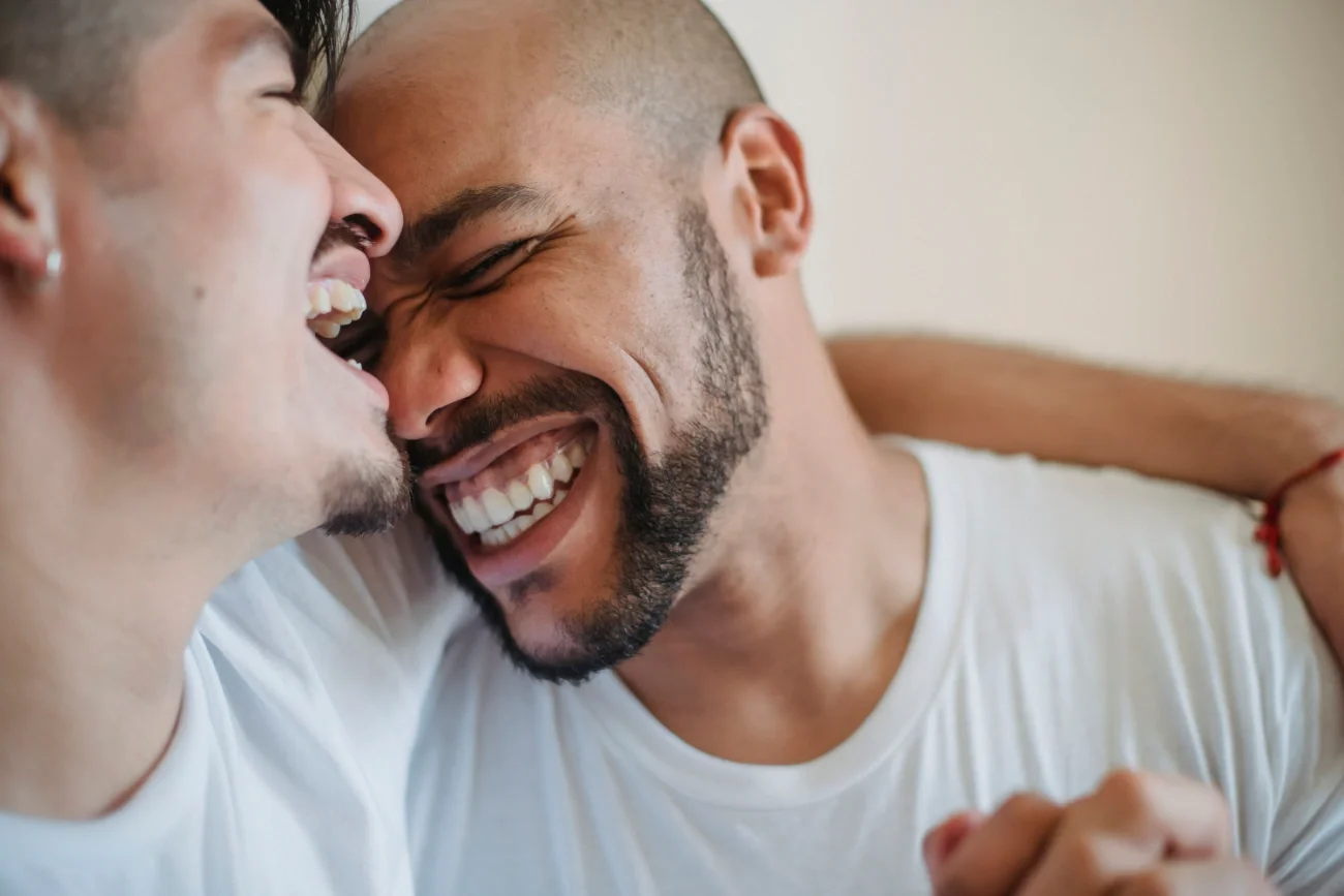 A man laughing and leaning into his boyfriend.