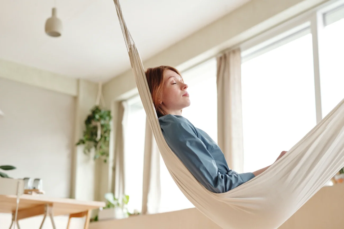 A woman laying down on a hammock indoors, relaxing.