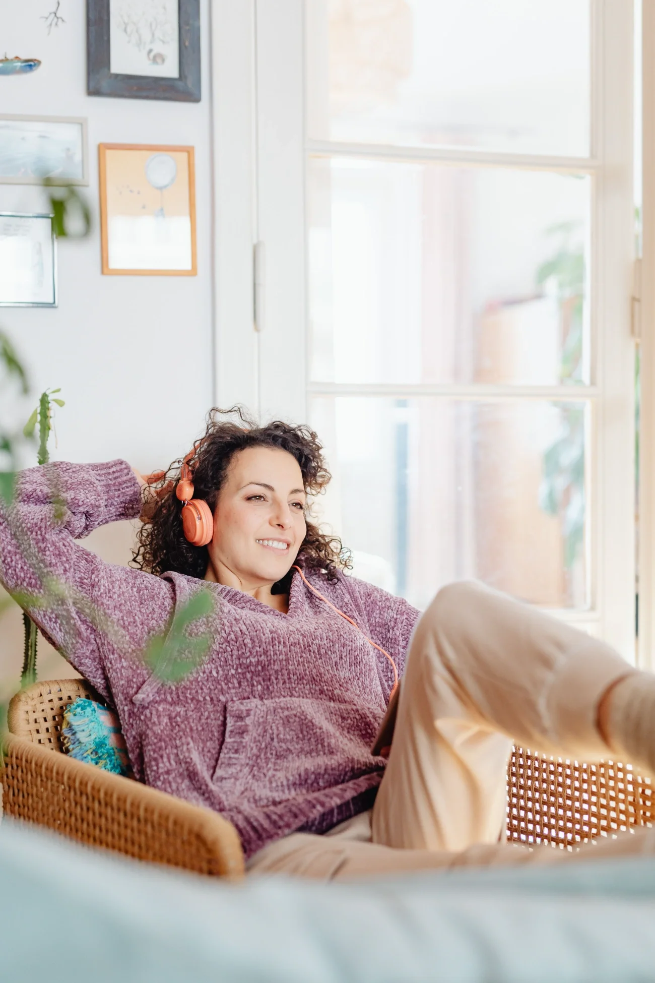 A woman sitting on a woven chair wearing headphones and looking relaxed.