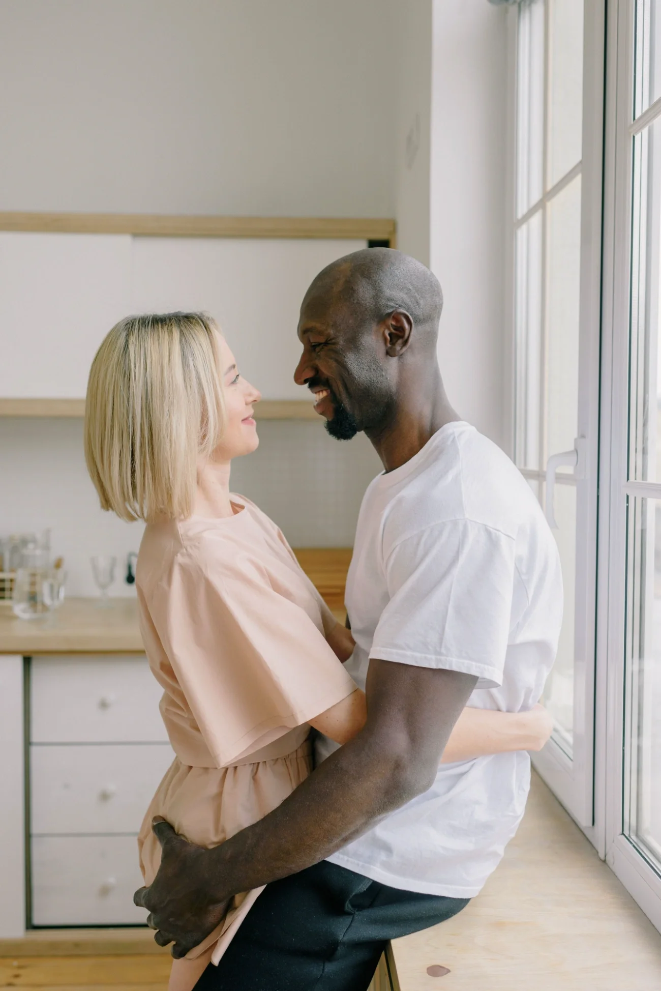 A couple embracing each other and smiling at each other in a kitchen.