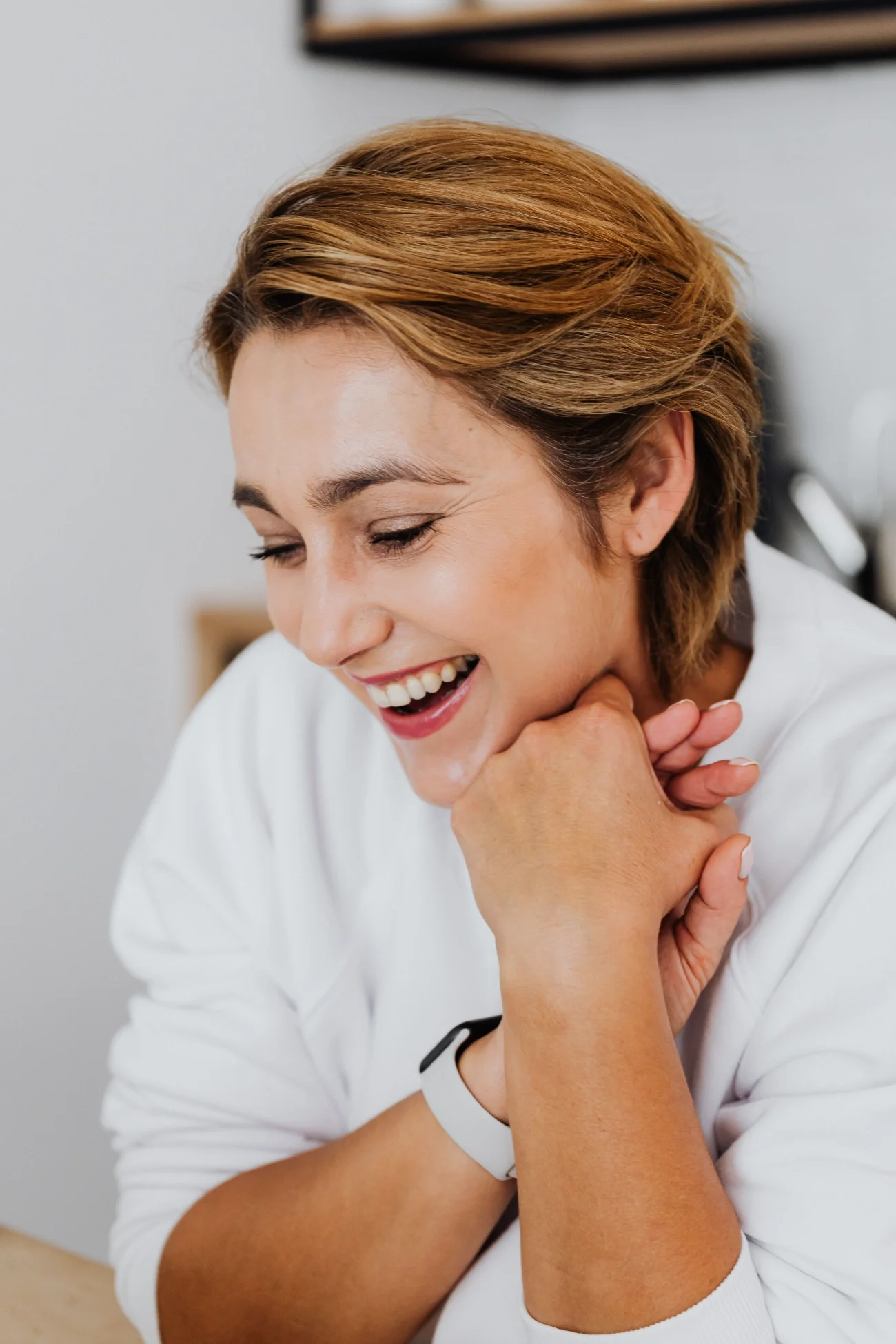 A woman laughing, looking down, with her hands joined together by her face.