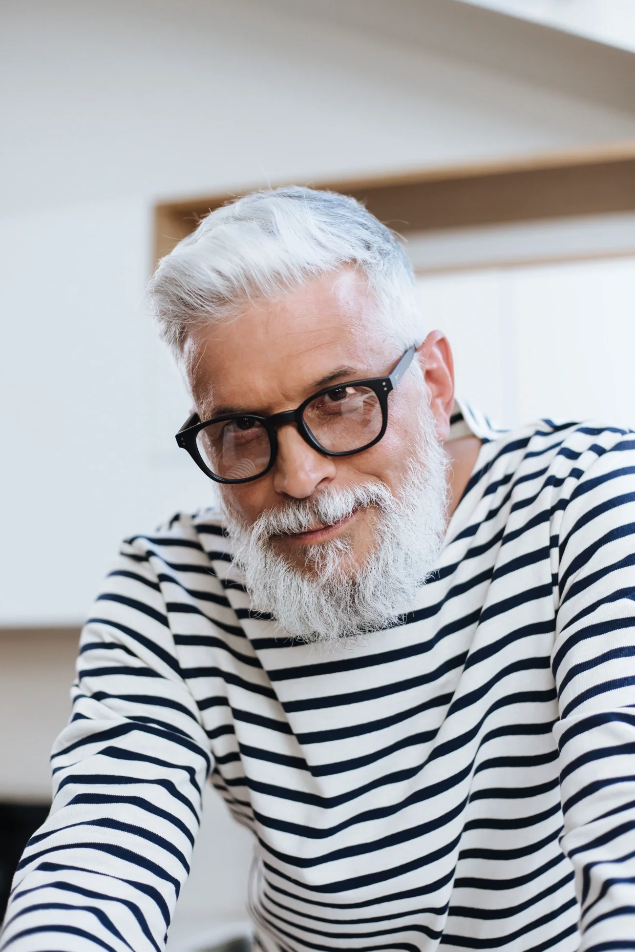 An older man with glasses and a striped shirt smiling at the camera.