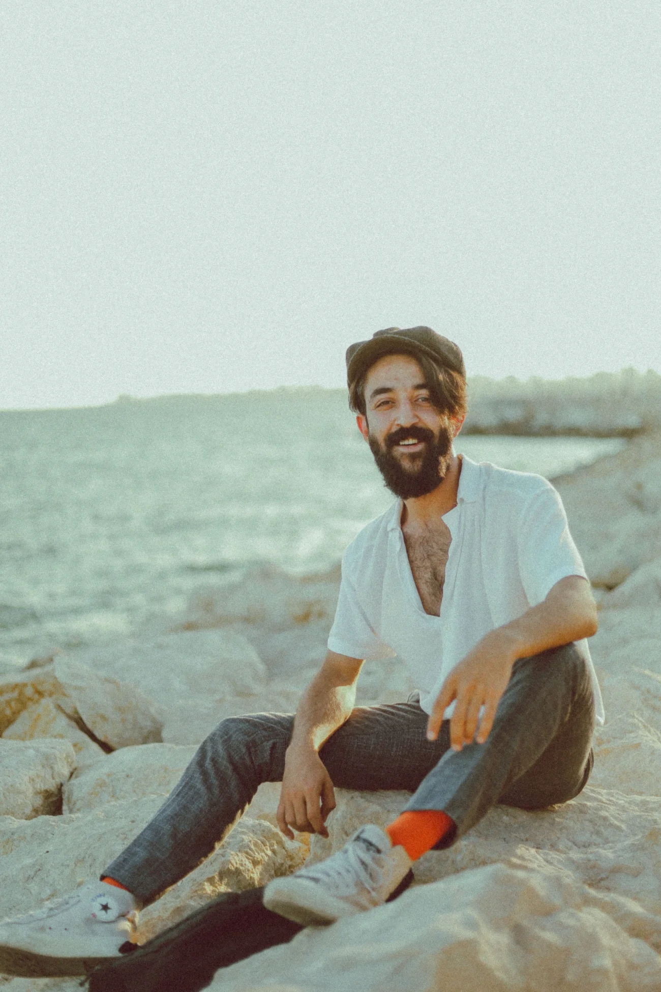 A man smiling at the camera, sitting on rocks by a lake.